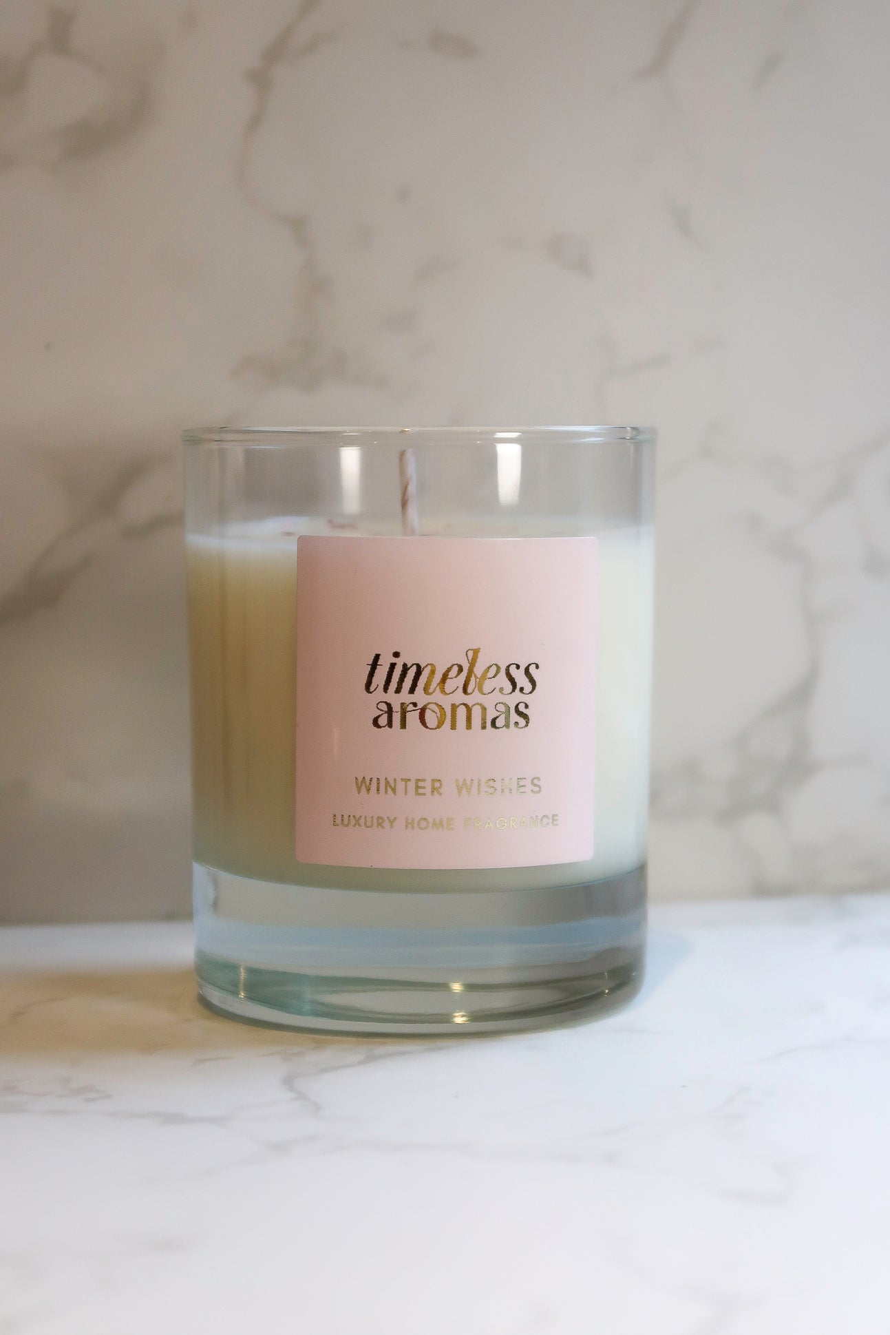 A beautiful Timeless Aromas Winter Wishes luxury scented candle displayed on a marble surface, showcasing its elegant design and soft glow.