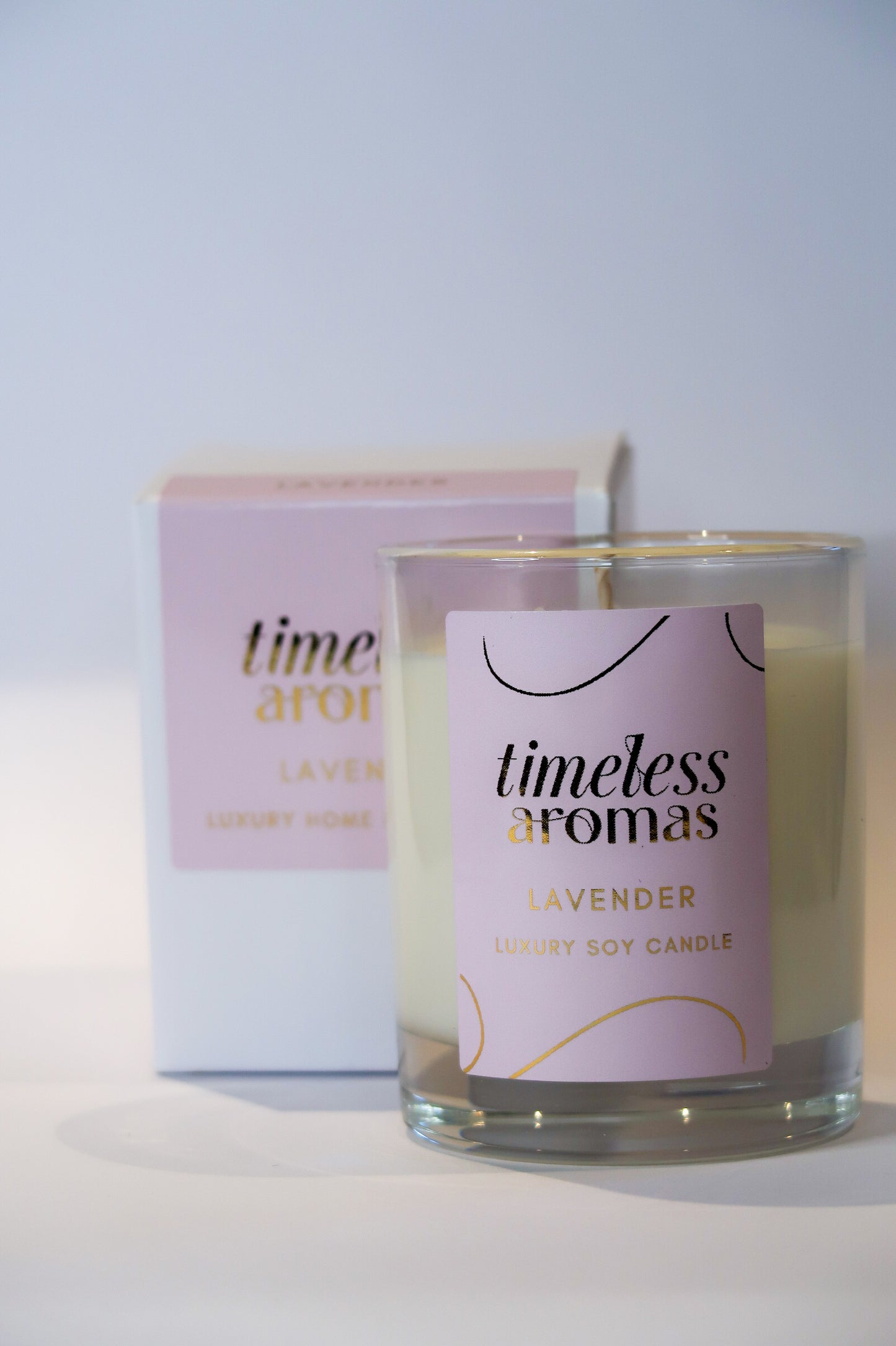 Lavender Luxury Scented Candle by Timeless Aromas, showcasing a clear glass jar with a pink label, set against a minimalist background.
