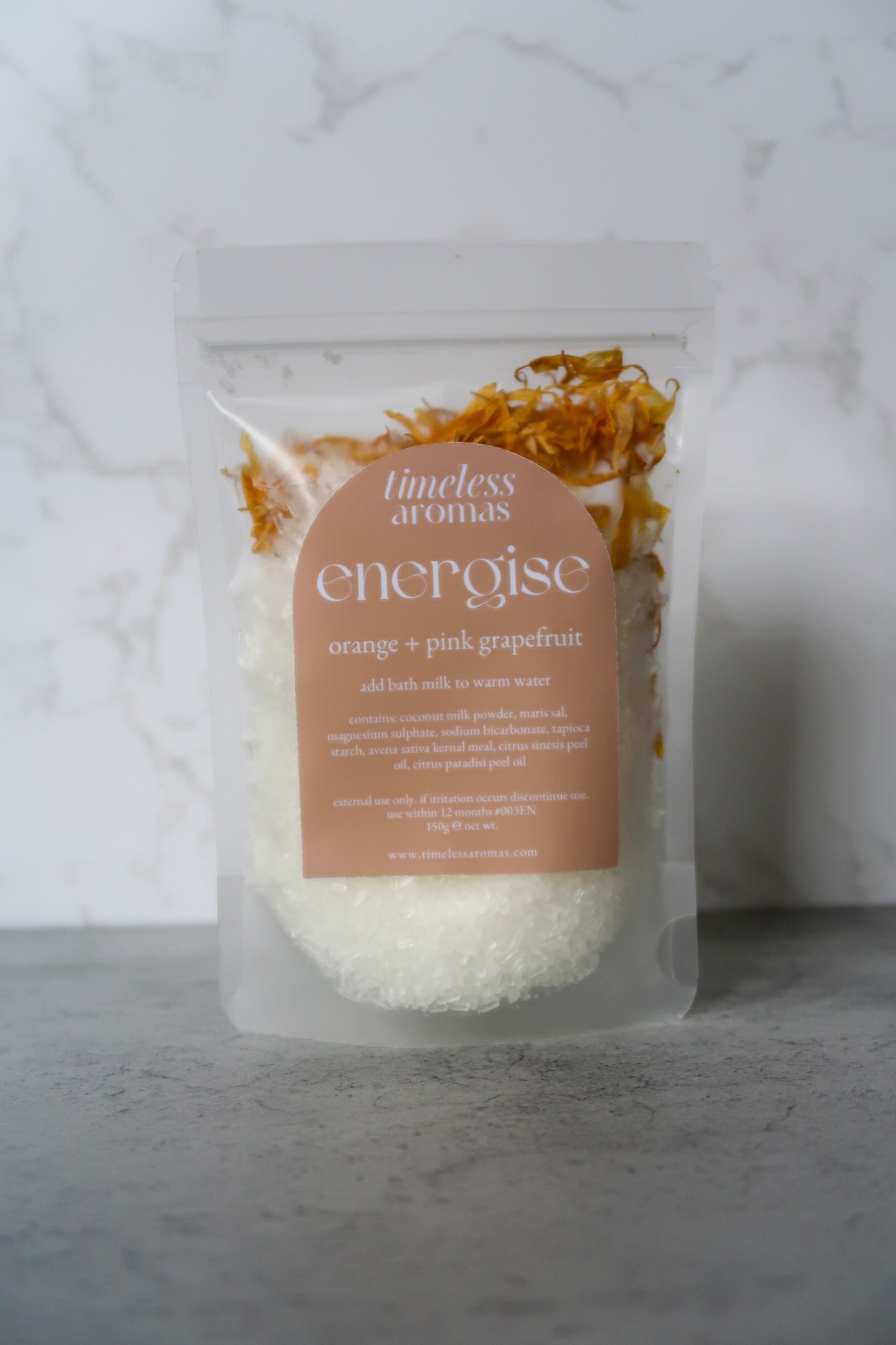 Timeless Aromas Energise Bath Milk featuring a package filled with a blend of coconut milk, salts, and floral accents. Ideal for a rejuvenating soak, this energise vegan bath milk combines sweet orange and pink grapefruit essential oils.