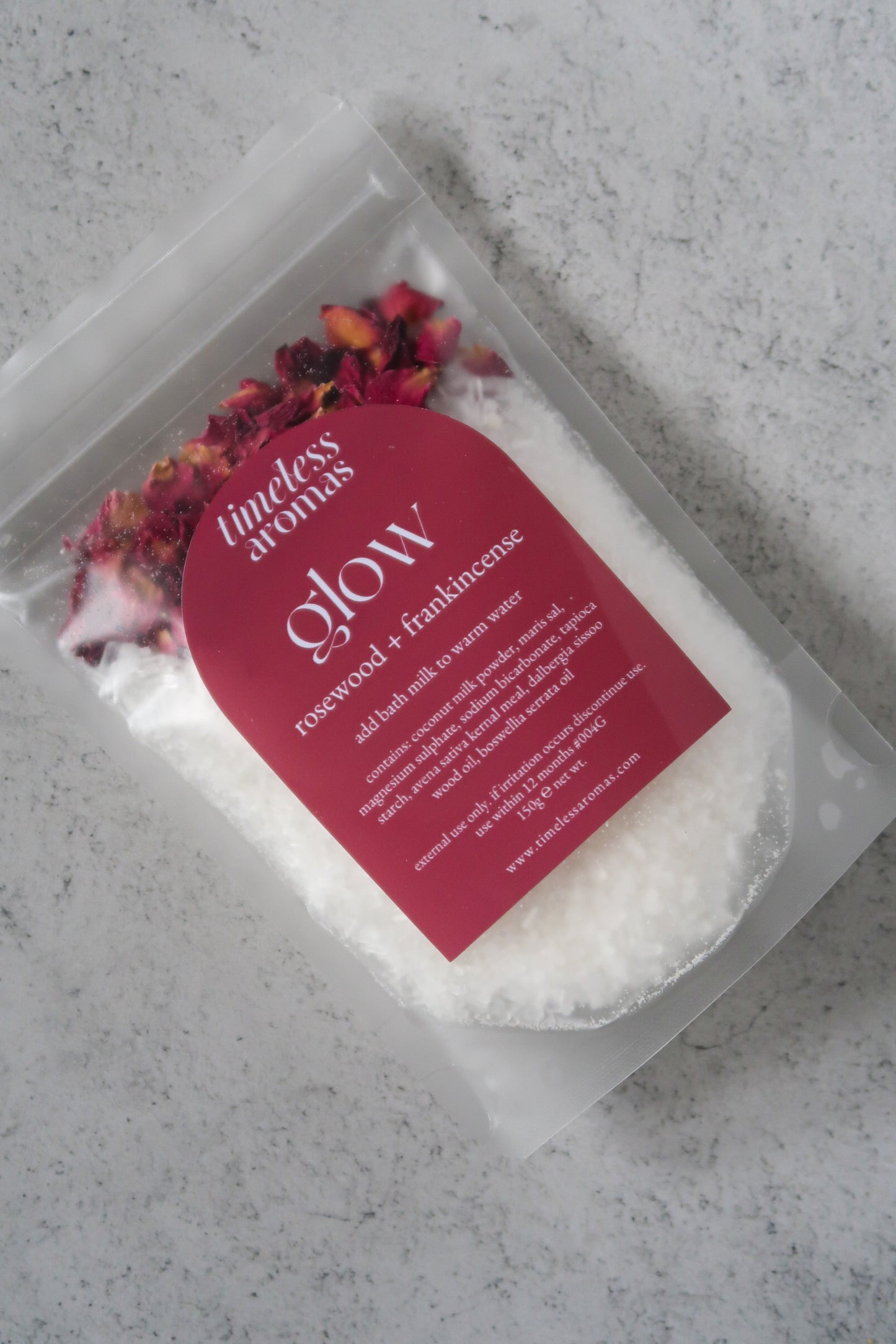 Timeless Aromas Glow Bath Milk in a clear pouch, showcasing the rosewood and frankincense ingredients, highlighted as a glow vegan bath milk for relaxing baths.