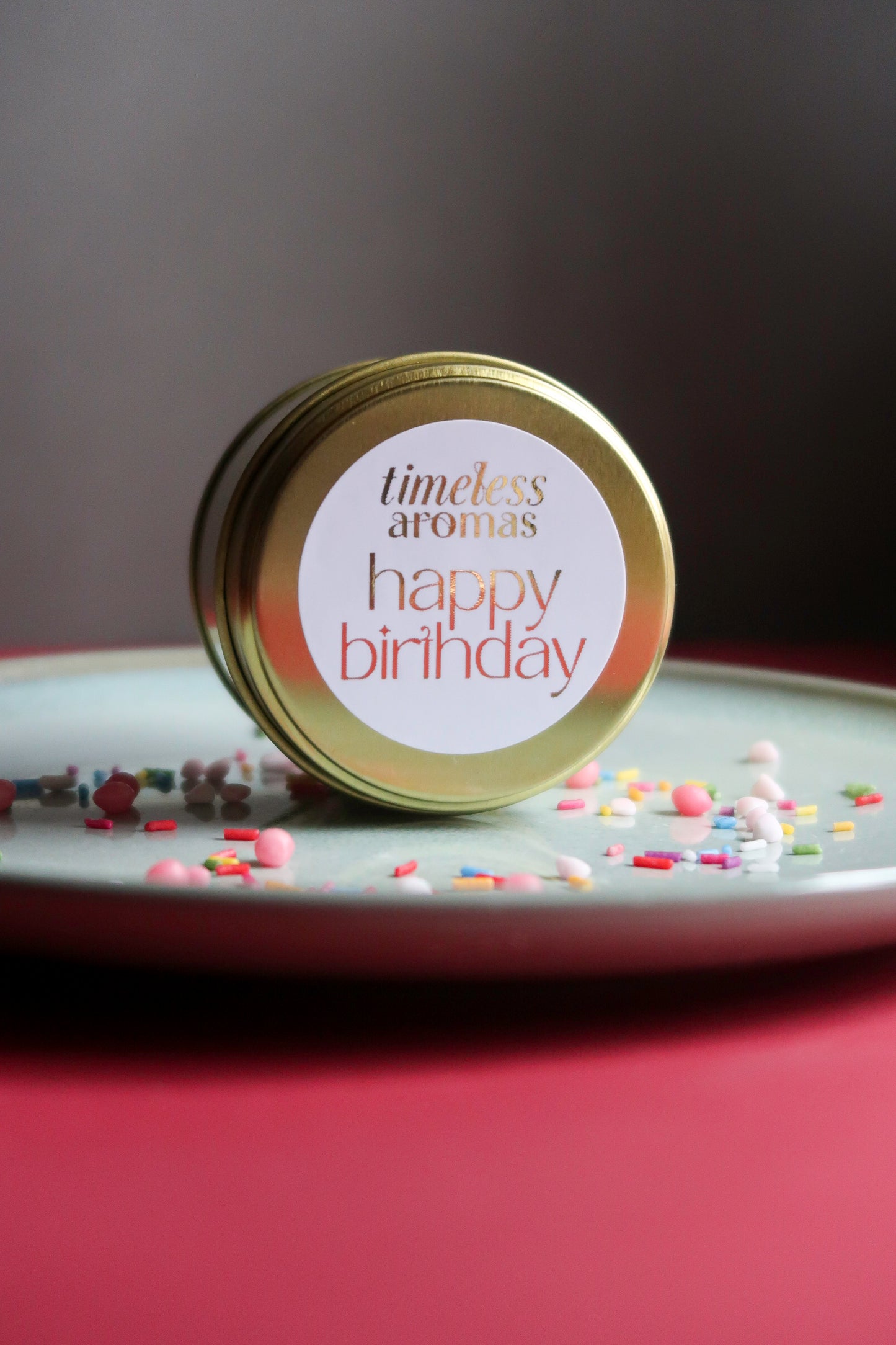 Happy Birthday Travel Tin Candle artwork from Timeless Aromas positioned attractively with sprinkles, a delightful birthday tin candle gift idea.