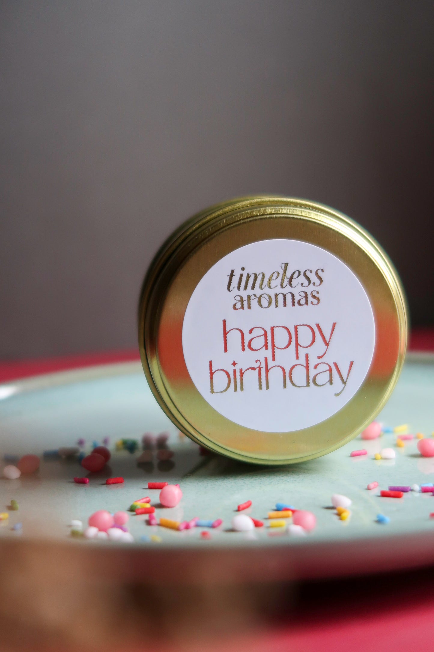 Happy Birthday Travel Tin Candle from Timeless Aromas on a plate decorated with colorful sprinkles, perfect as a birthday tin candle gift.