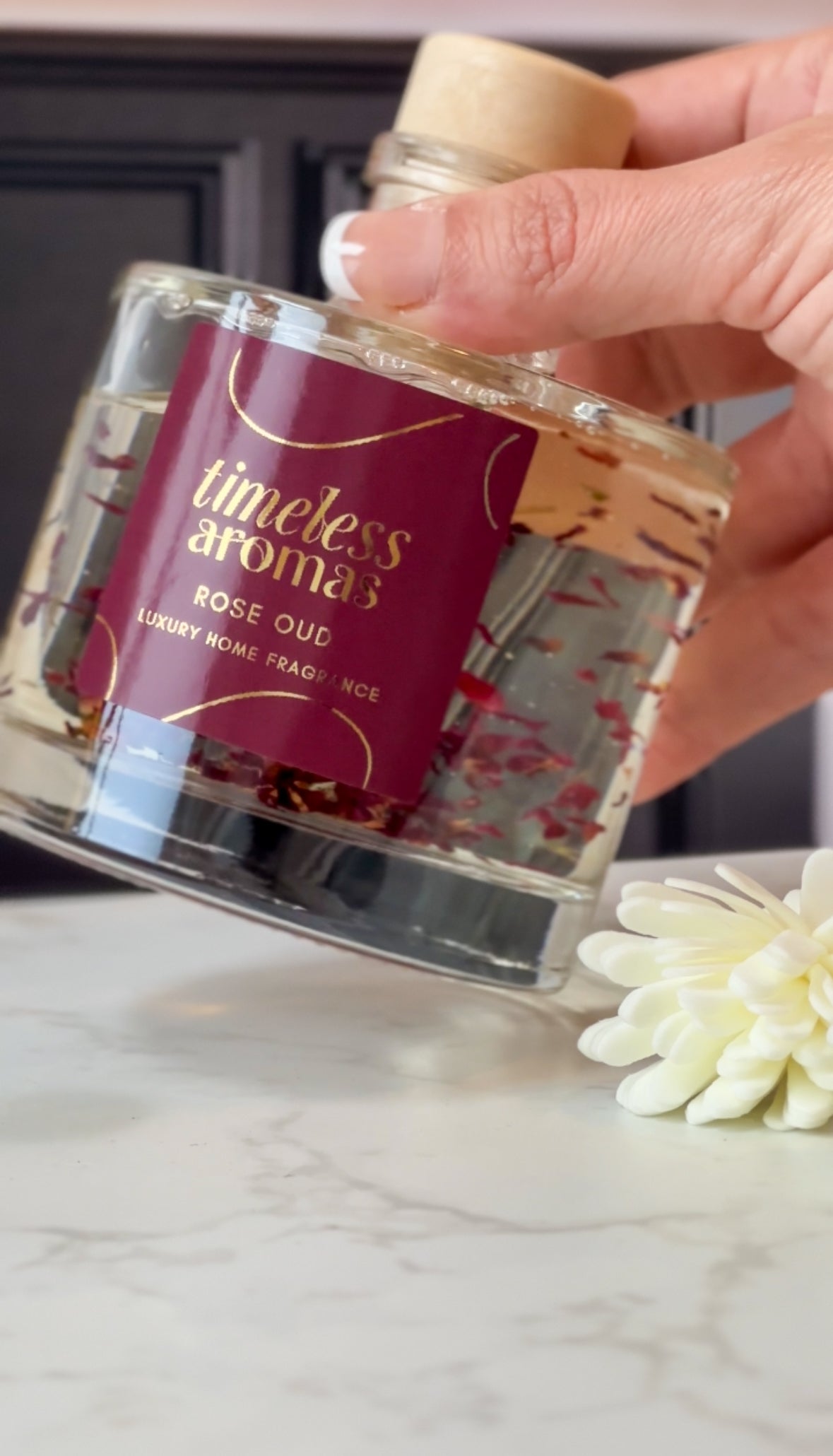 A closer look at the Timeless Aromas Rose Oud Luxury Reed Diffuser being held, highlighting its elegant label and beautiful floral accents, ideal for any decor.