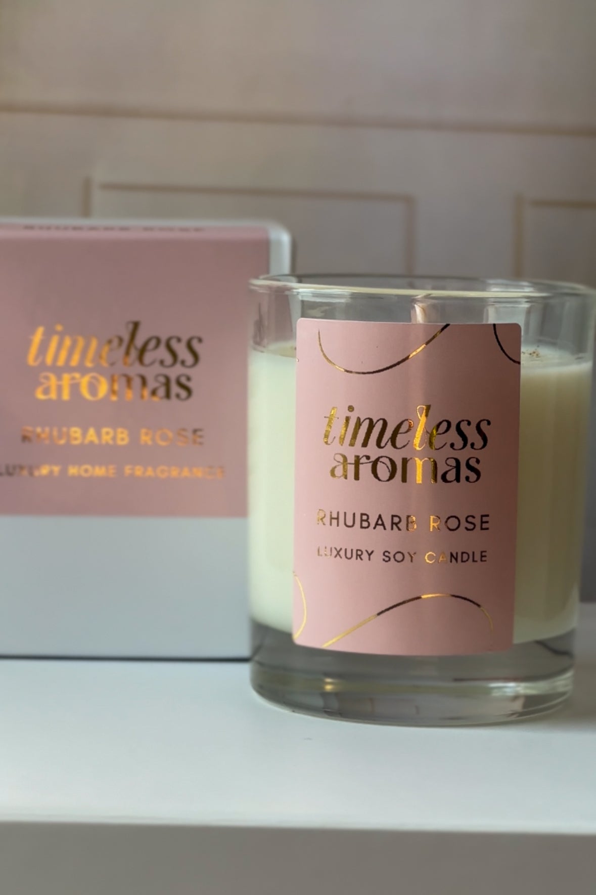 Timeless Aromas Rhubarb Rose Luxury Candle - 200g alongside its stylish packaging, emphasizing its luxury appeal. Ideal for gifting or enhancing your space with the enchanting scent of this rhubarb rose luxury scented candle.