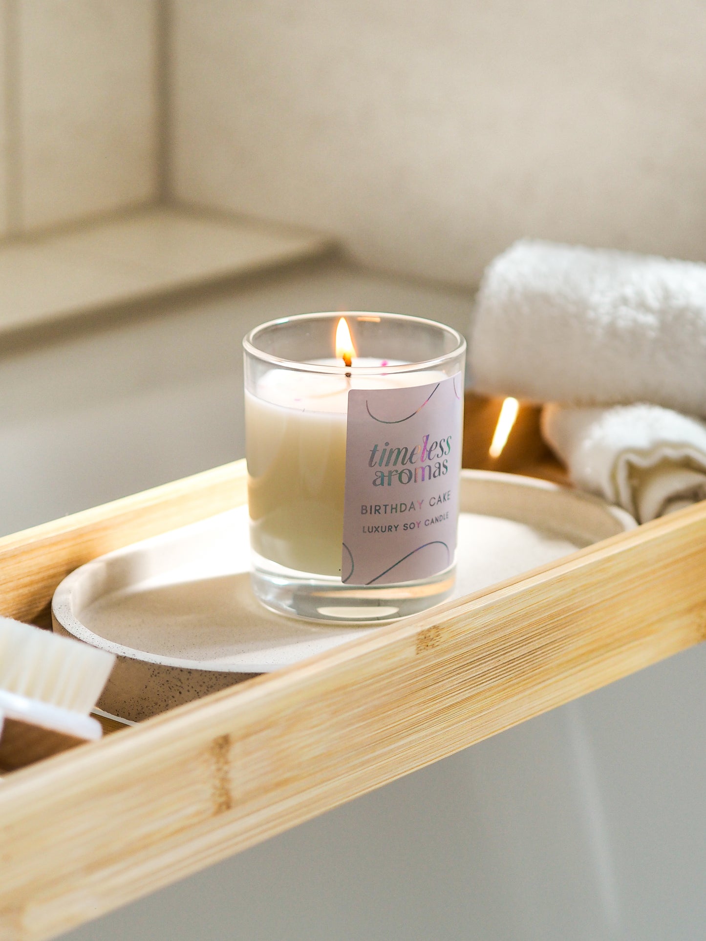 Timeless Aromas Birthday Cake Scented Candle flickering on a bamboo bath tray, creating a relaxing ambiance while indulging in a sweet aroma.