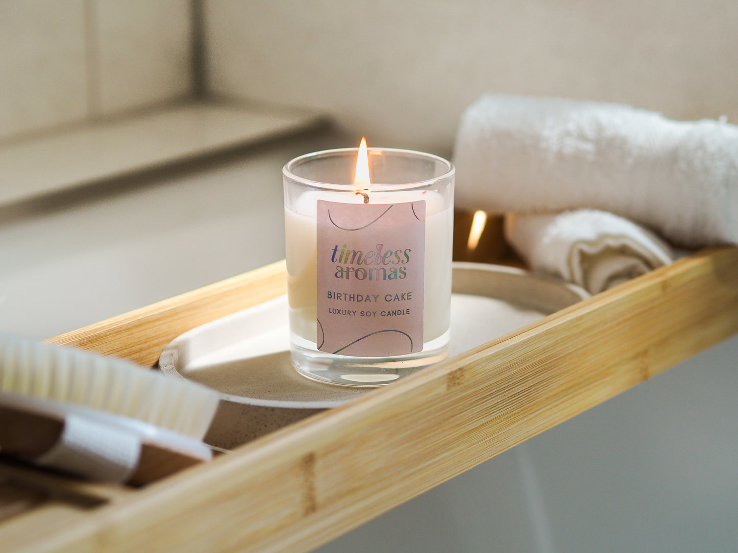Close-up of Timeless Aromas Birthday Cake Scented Candle lit on a bamboo bath tray, showcasing its luxurious scent designed for comfort.