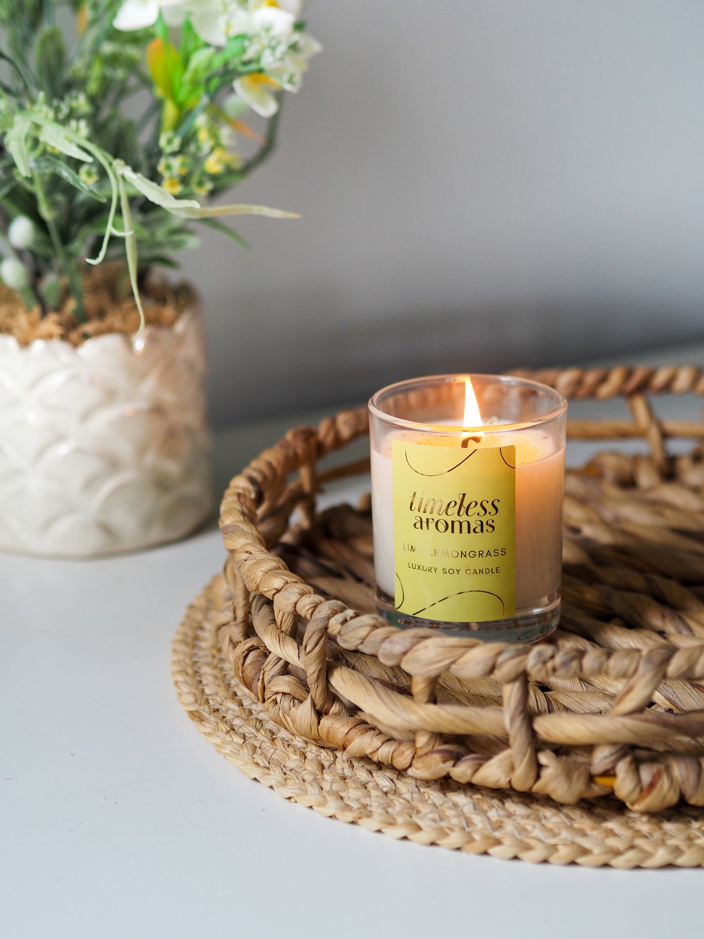 The vibrant Lime Lemongrass Luxury Candle by Timeless Aromas displayed on a woven tray with fresh flowers, adding a fresh fragrance to the room.