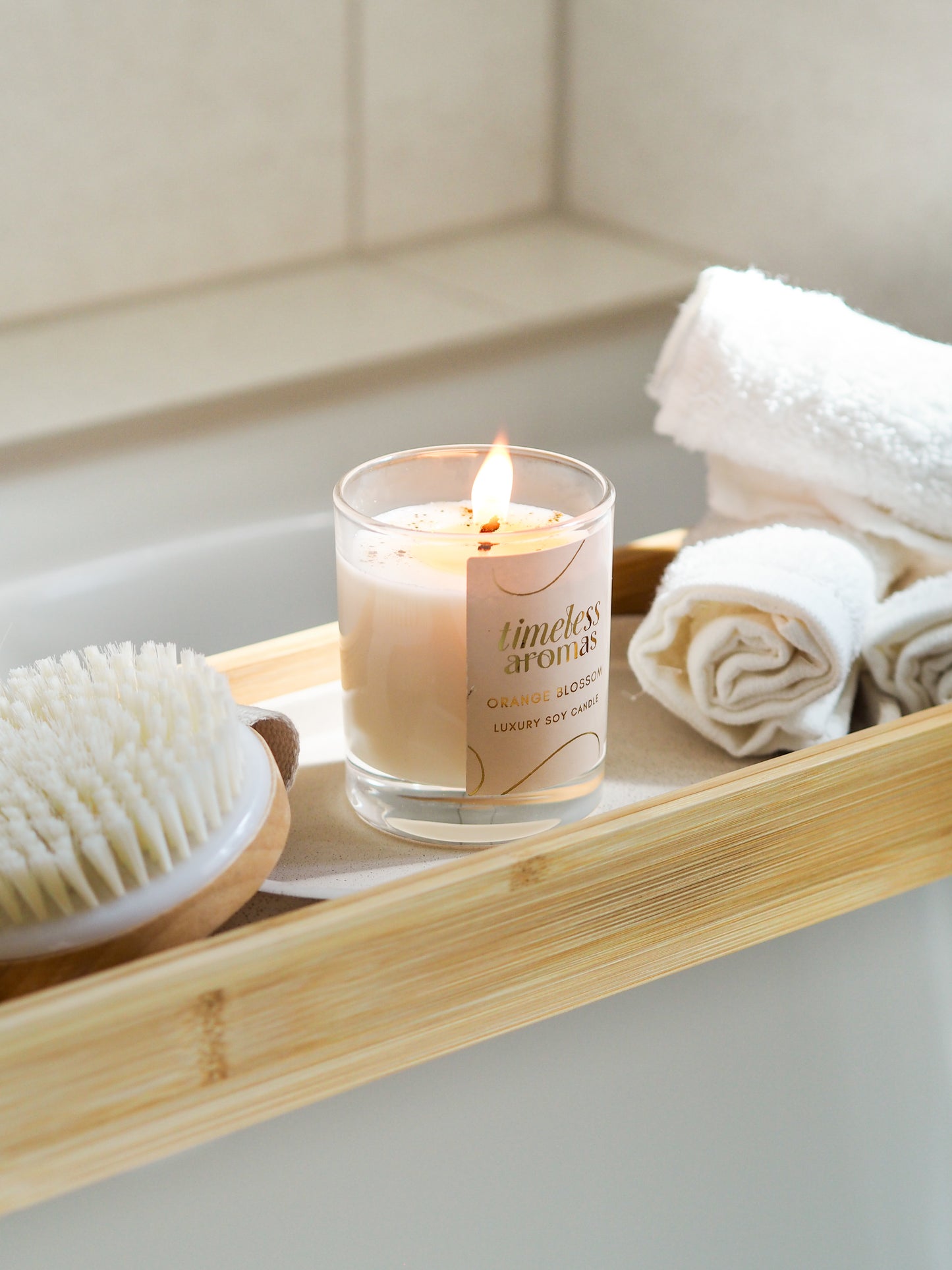 Orange Blossom Luxury Candle by Timeless Aromas placed in a tranquil bathroom setting, surrounded by towels and a brush, ideal for relaxation.