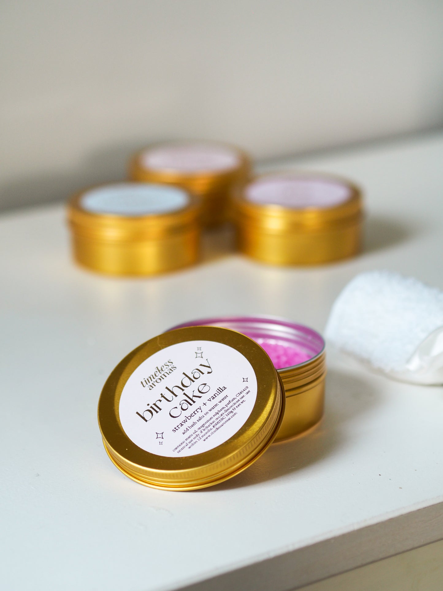 Close-up of Timeless Aromas Birthday Cake Gold Tin Bath Salts – Strawberry Sweets, showcasing the pink bath salts perfect for relaxation in your self-care routine.