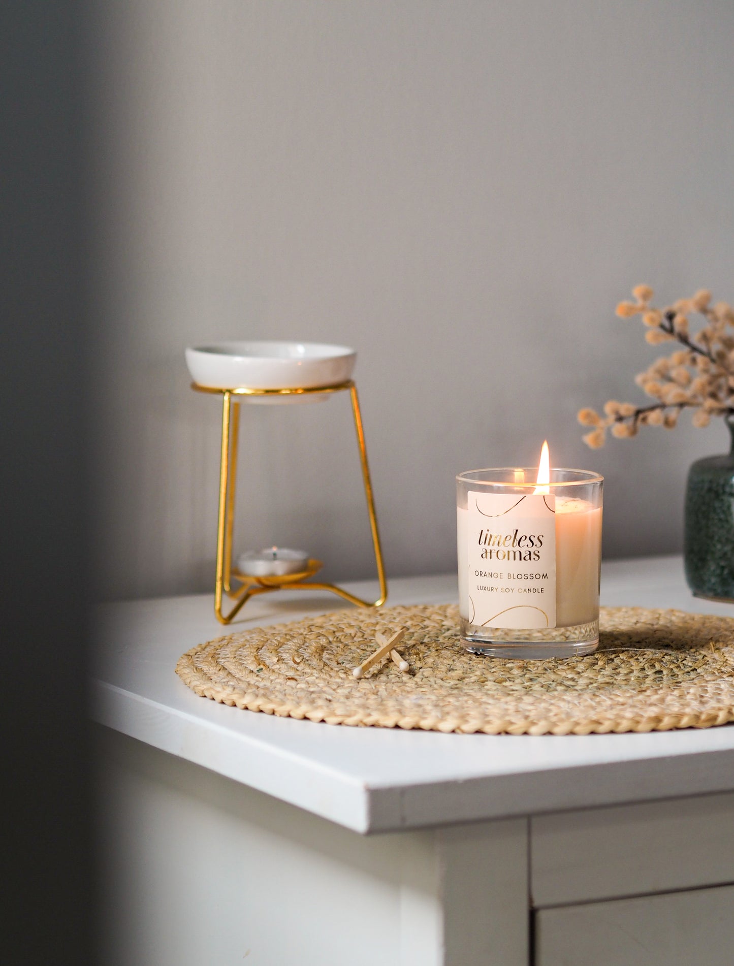The Orange Blossom Luxury Candle by Timeless Aromas lit on a stylish table setting, featuring a natural woven placemat, perfect for creating a calming atmosphere.