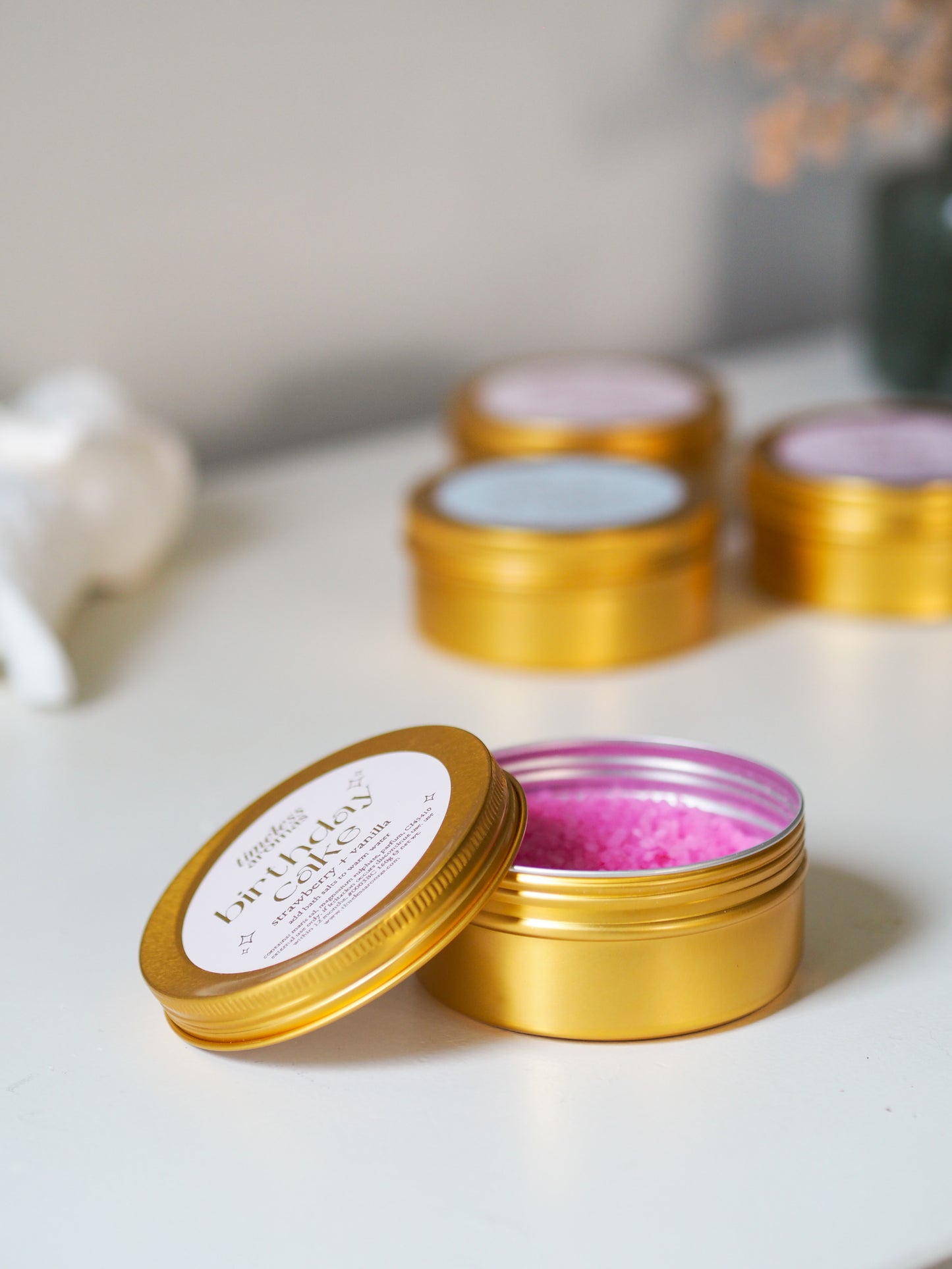 Open tin of Timeless Aromas Birthday Cake Gold Tin Bath Salts – Strawberry Sweets, offering a peek at the delightful pink salts ideal for a relaxing bath experience.