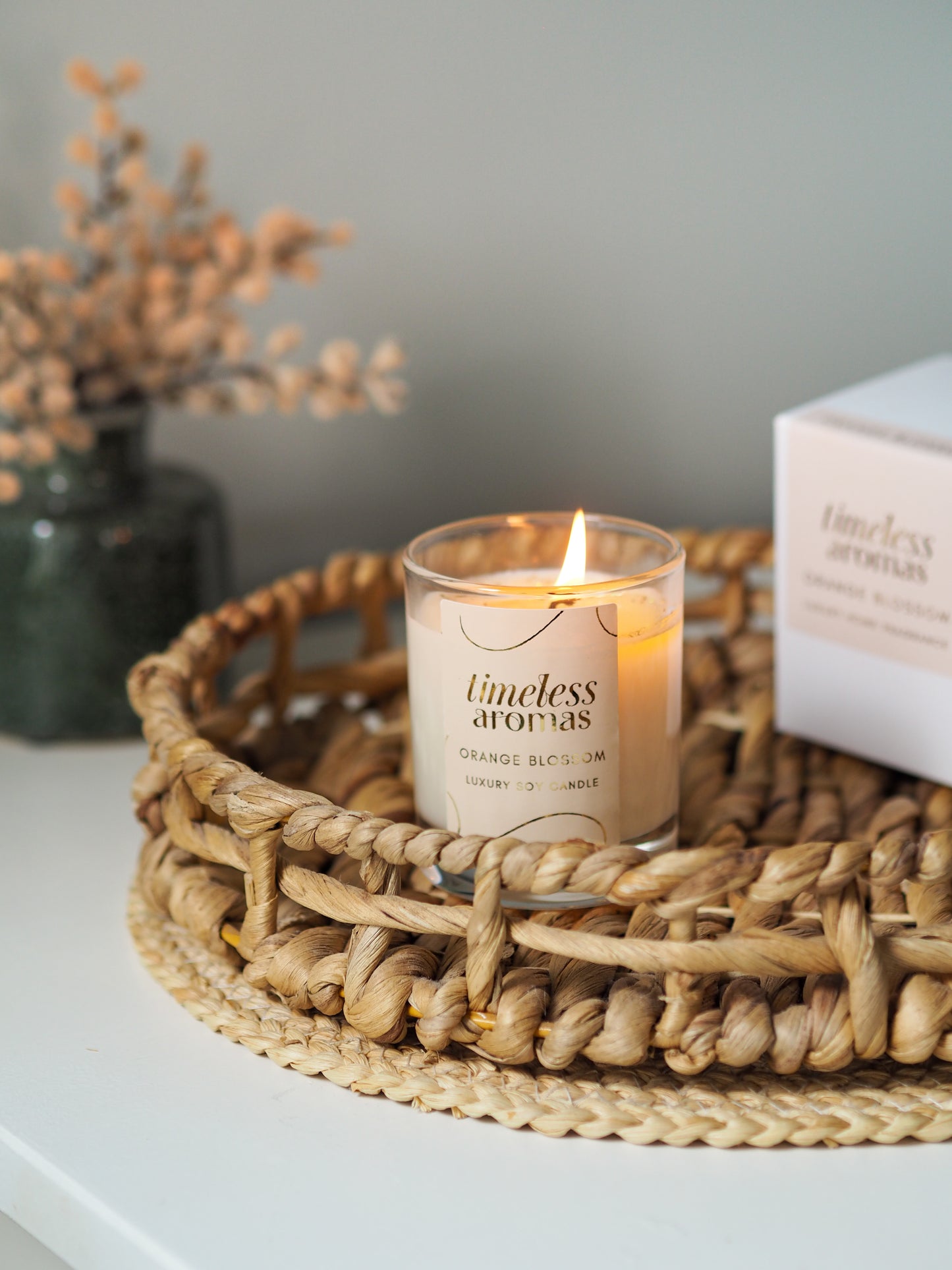 The Orange Blossom Luxury Candle by Timeless Aromas displayed on a woven tray, emphasizing its delicate floral fragrance and stylish packaging.