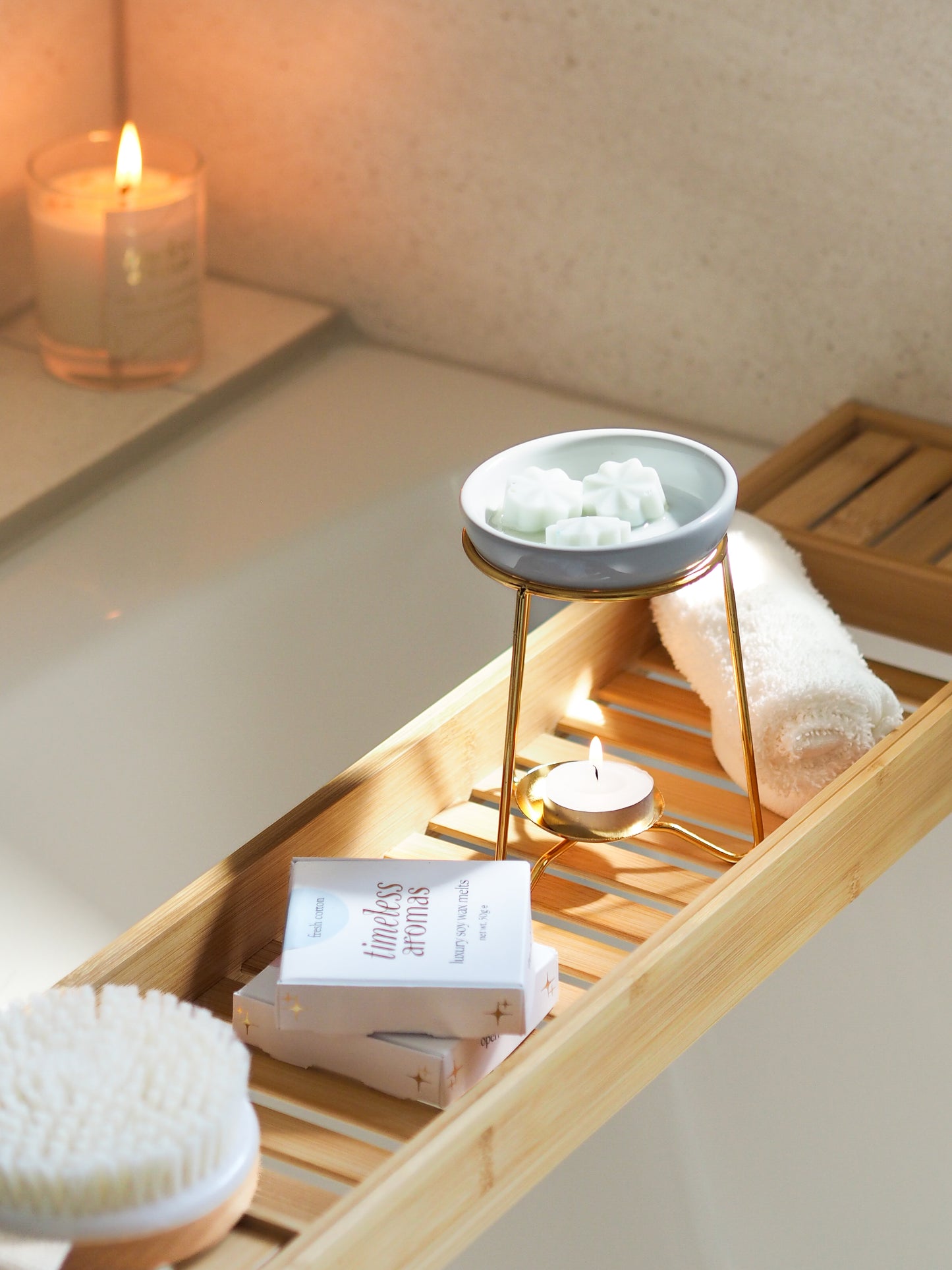 A luxury wax melt burner in a serene bath setting, showcasing a gold frame and ceramic dish, surrounded by candles and bath essentials, by Timeless Aromas.