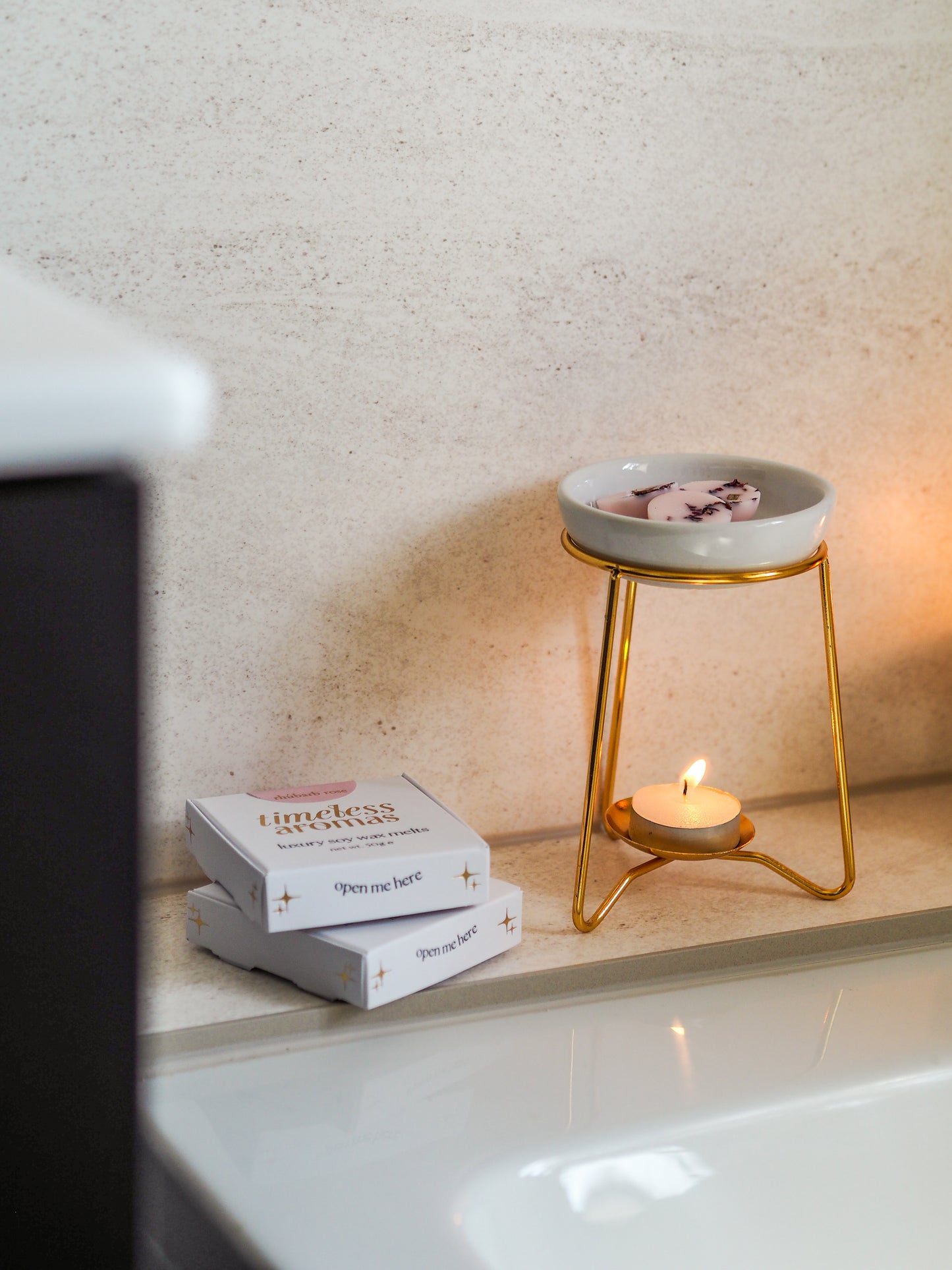 Beautifully arranged luxury wax melt burner with a gold frame and white ceramic dish on a bathroom countertop, highlighting scented wax melts by Timeless Aromas.