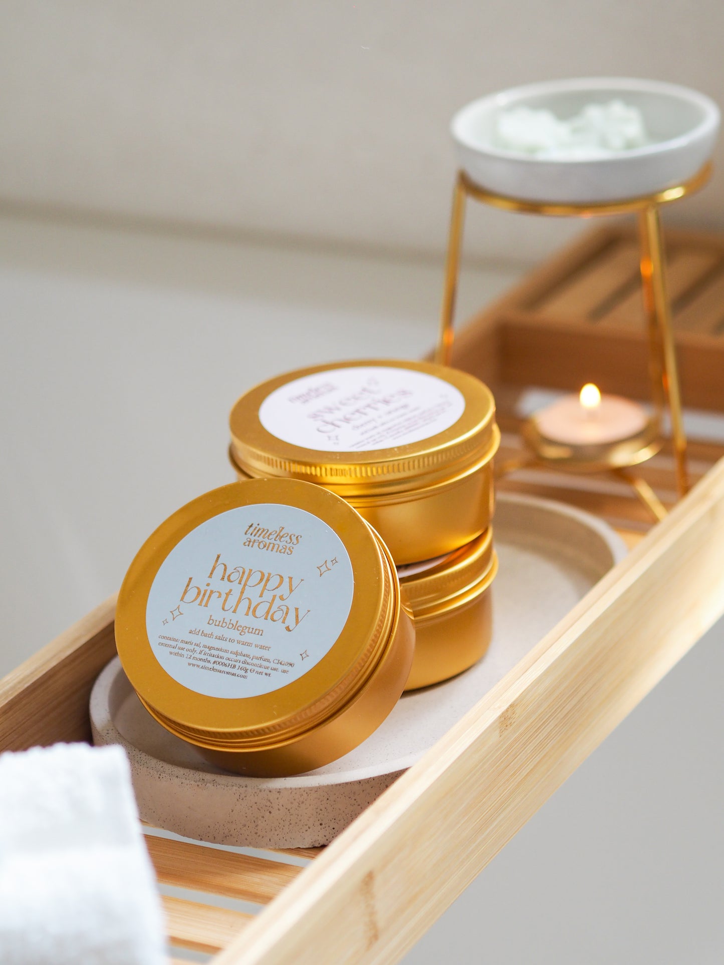 Happy Birthday Gold Tin Bath Salts by Timeless Aromas, featuring vibrant golden tins on a bamboo tray, perfect bath salts for relaxation with a bubblegum fragrance.