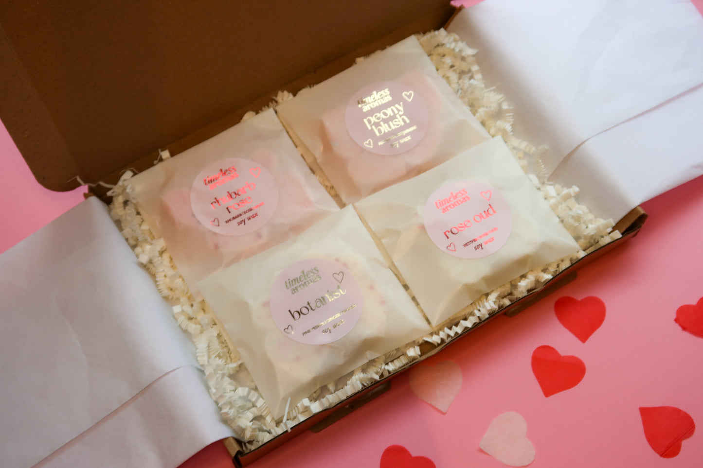 Timeless Aromas Pink Wax Melt Gift Set showcasing four scented soy wax melts: Rhubarb Rose, Peony Blush, Rose Oud, and Botanist, elegantly arranged in a gift box with pink tissue paper.
