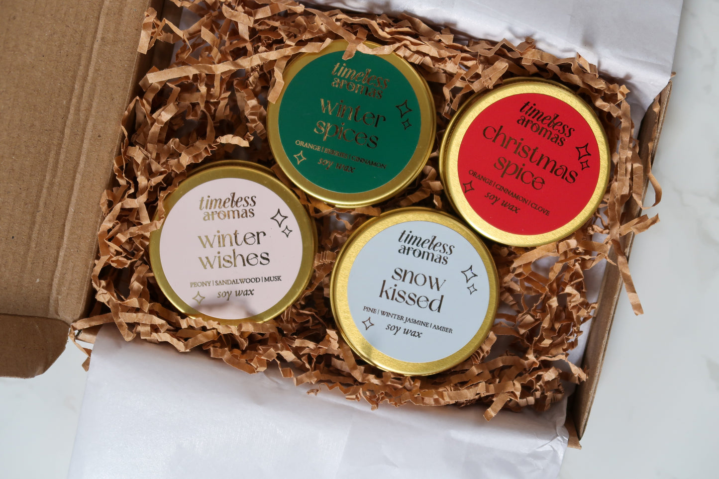 Exquisite Mini Christmas Candle Gift Set by Timeless Aromas, displaying four enchanting gold tin candles with labels showcasing festive scents including Winter Wishes and Snow Kissed.
