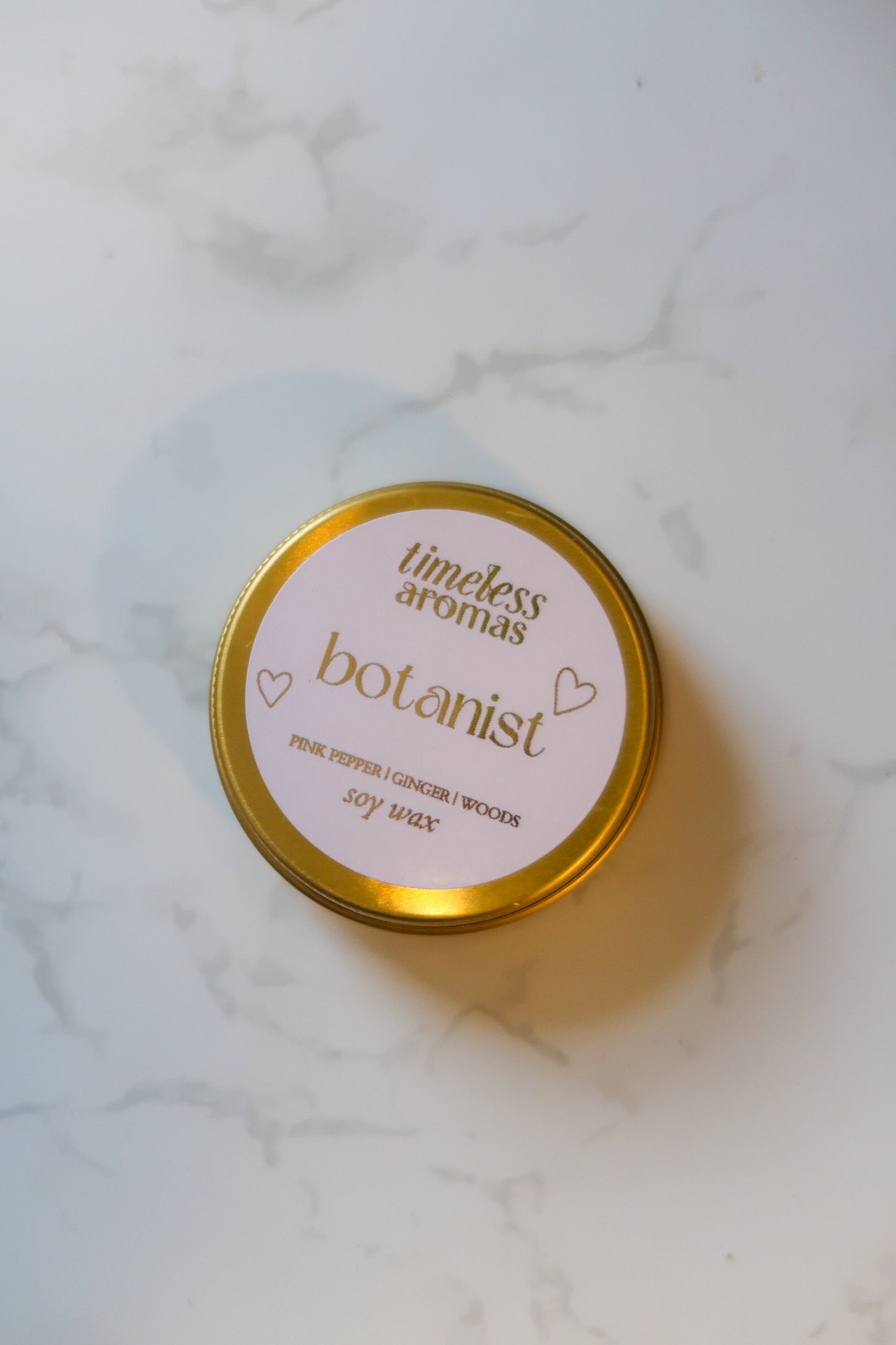 Top view of the Botanist Mini Gold Tin Candle by Timeless Aromas Ltd, displaying its lovely gold tin and simple design, an excellent example of a floral and woody mini gold tin candle.