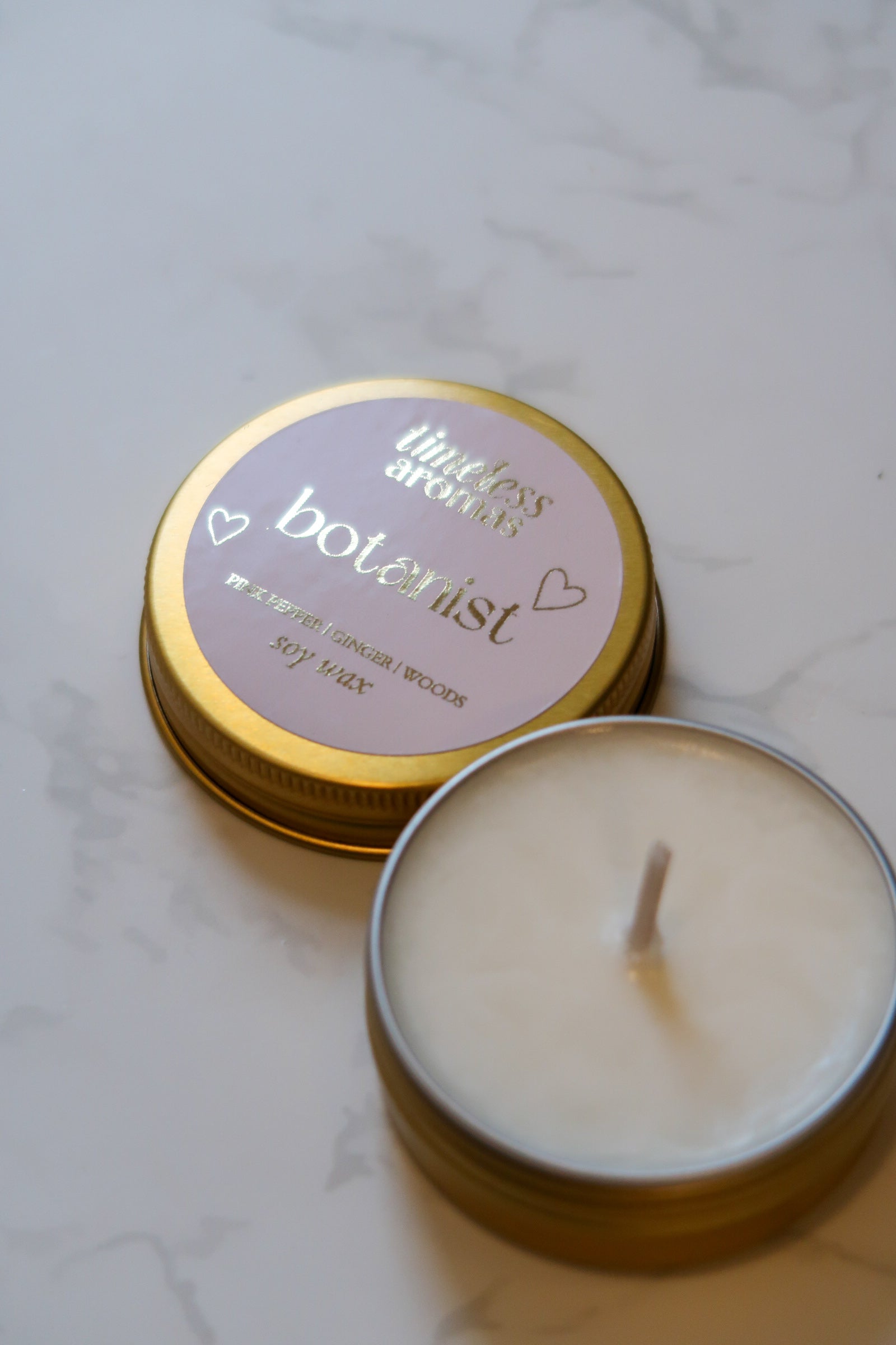 Another view of the Botanist Mini Gold Tin Candle by Timeless Aromas Ltd, highlighting the elegant design and inviting aroma, suitable as a floral and woody mini gold tin candle.