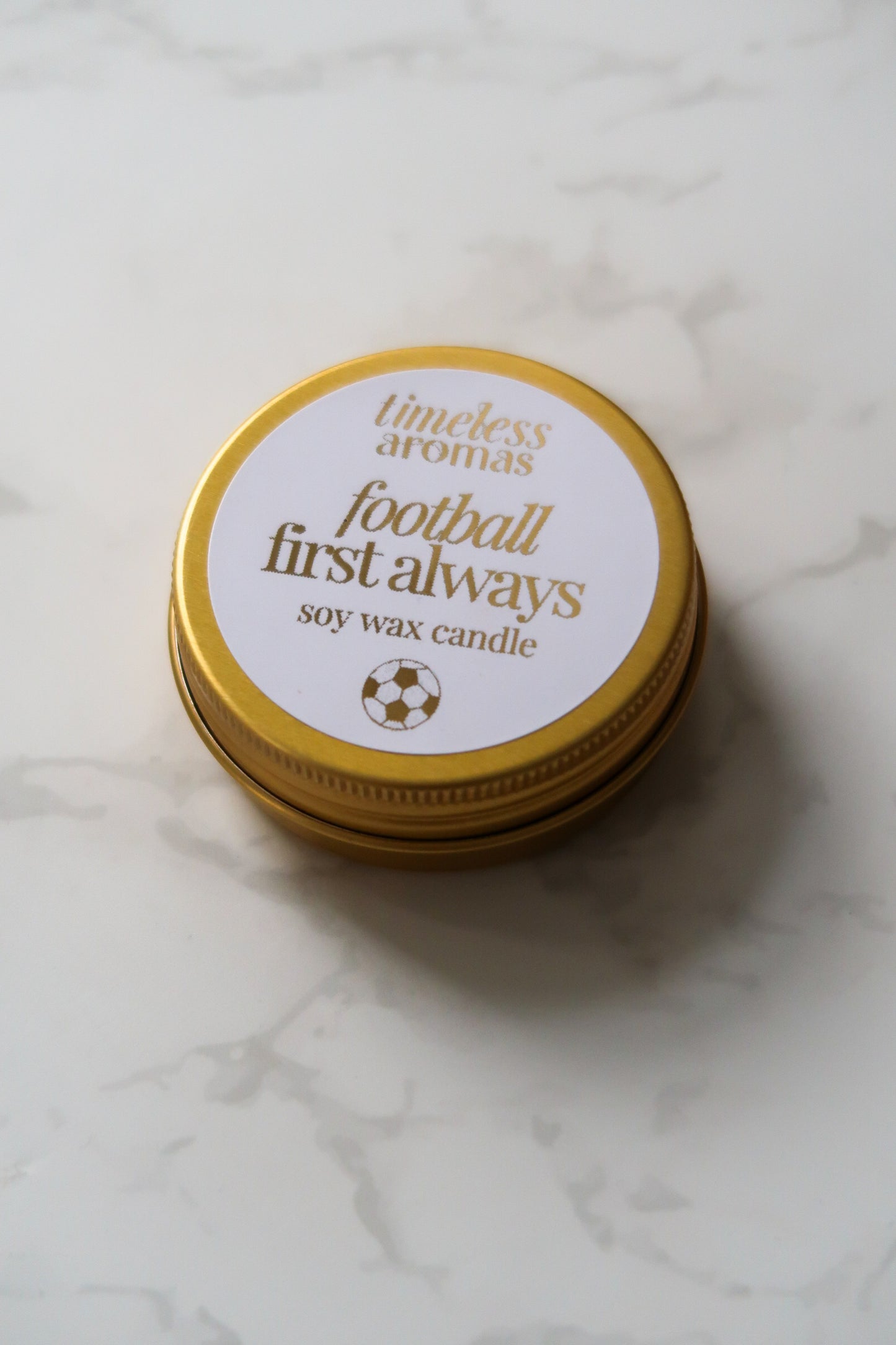 Timeless Aromas Ltd Football First Always Mini Gold Tin Candle from a top view, highlighting its sleek design. This mini gold tin candle is a perfect gift for football fans and a lovely way to celebrate occasions such as Father's Day, appealing to supporters of England and their favourite teams like Arsenal and Chelsea.