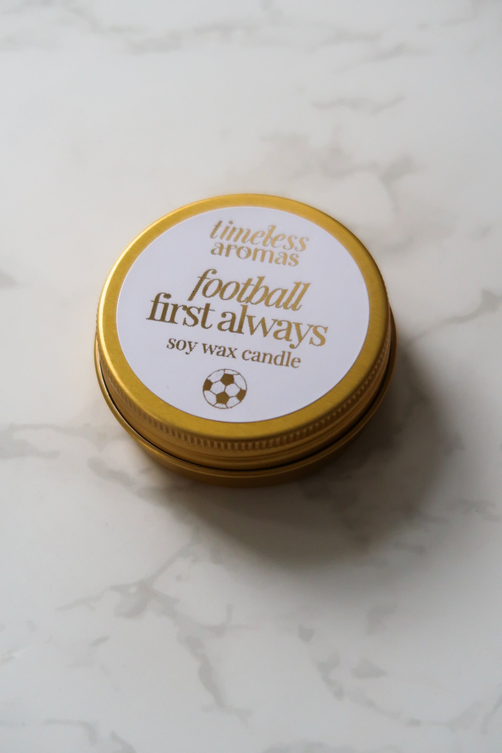 Timeless Aromas Ltd Football First Always Mini Gold Tin Candle from a top view, highlighting its sleek design. This mini gold tin candle is a perfect gift for football fans and a lovely way to celebrate occasions such as Father's Day, appealing to supporters of England and their favourite teams like Arsenal and Chelsea.