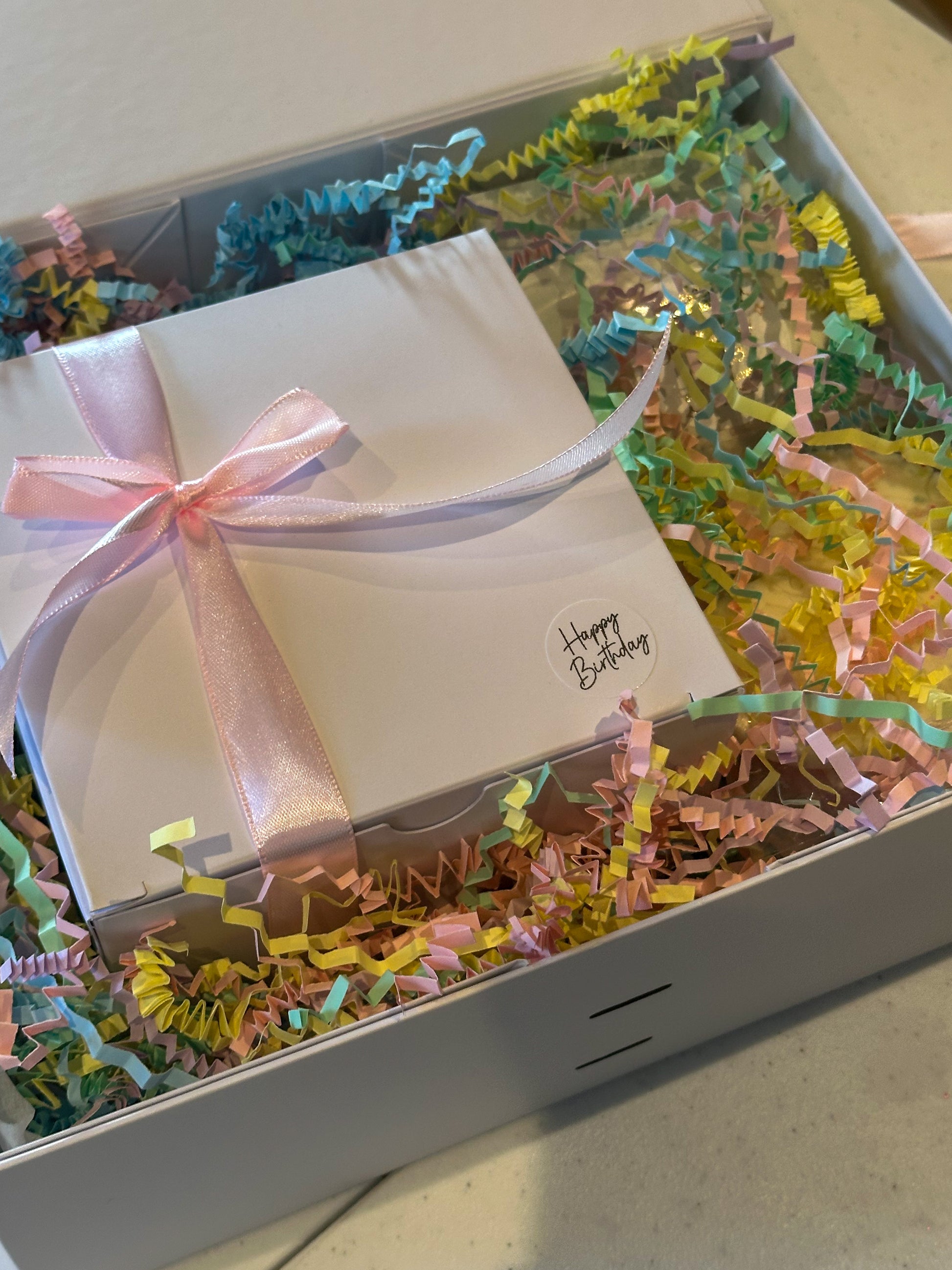 Beautifully packaged celebration mystery gift box from Timeless Aromas filled with colorful shredded paper and a 'Happy Birthday' gift inside, perfect for any celebration.