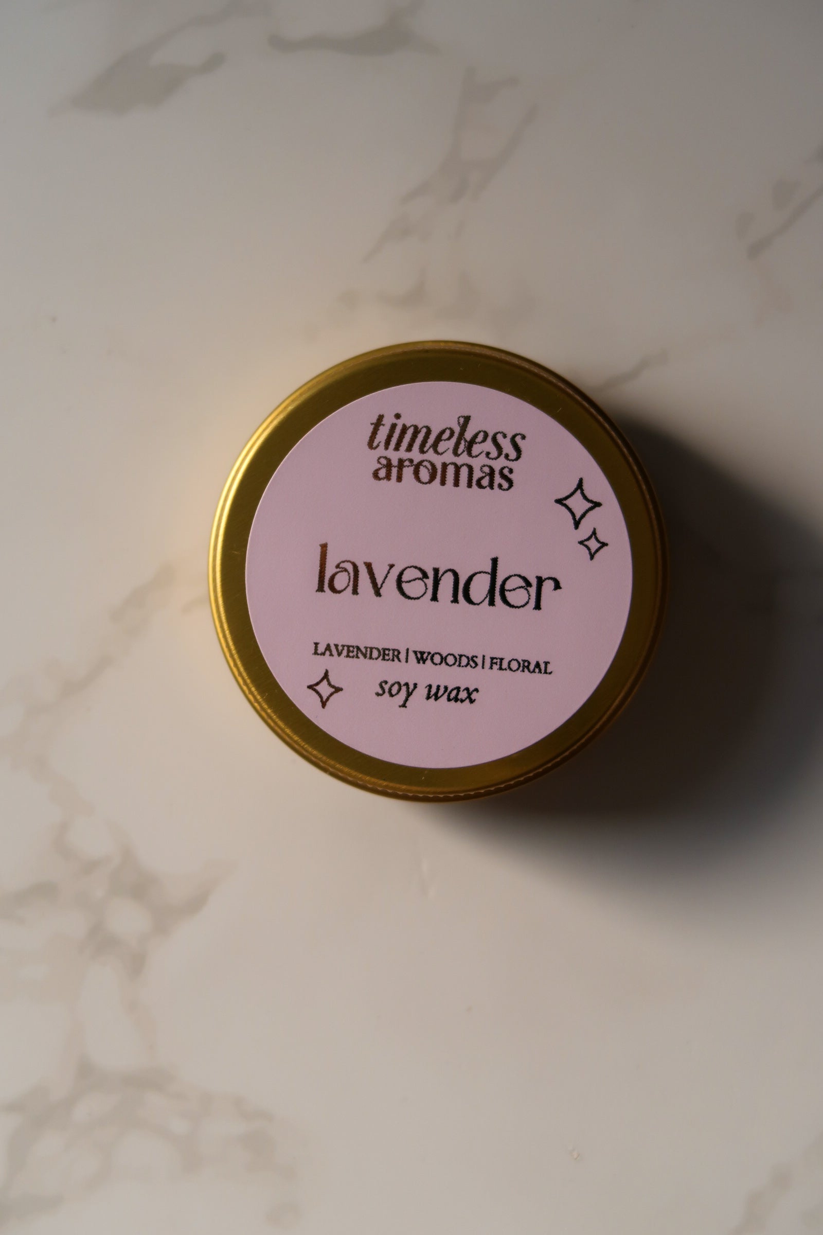 Top view of Lavender Mini Gold Tin Candle by Timeless Aromas, showcasing the pink label with the scent description, perfect for relaxation and home decor.