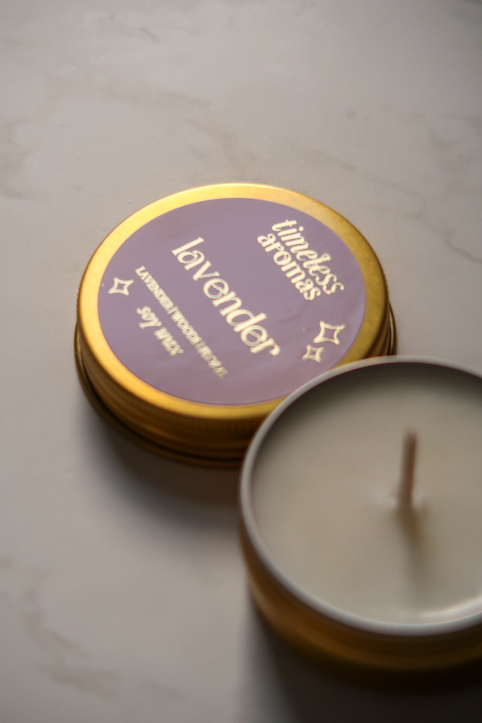Opened Lavender Mini Gold Tin Candle by Timeless Aromas, displaying the creamy soy wax and pink label, an elegant choice for creating a calming environment.