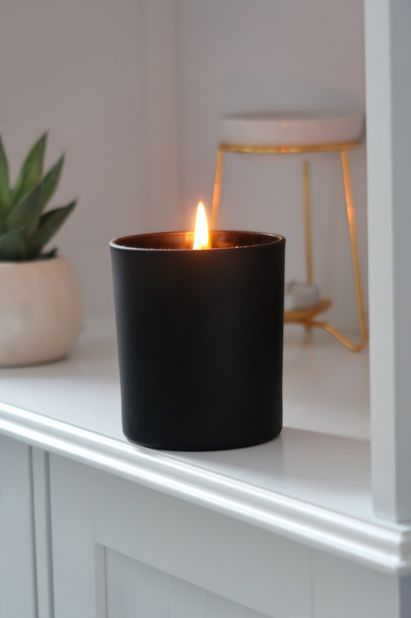 A lit 30cl Black Matte Candle from Timeless Aromas Ltd, showcasing the elegant design of a hand poured candle perfect for home fragrance. This ceramic jar candle adds a touch of style while being part of a pack of 6, making it an ideal gift. Features include a matte finish and blank label for customisation, perfect for wholesale. The white candle inside enhances the overall aesthetic.