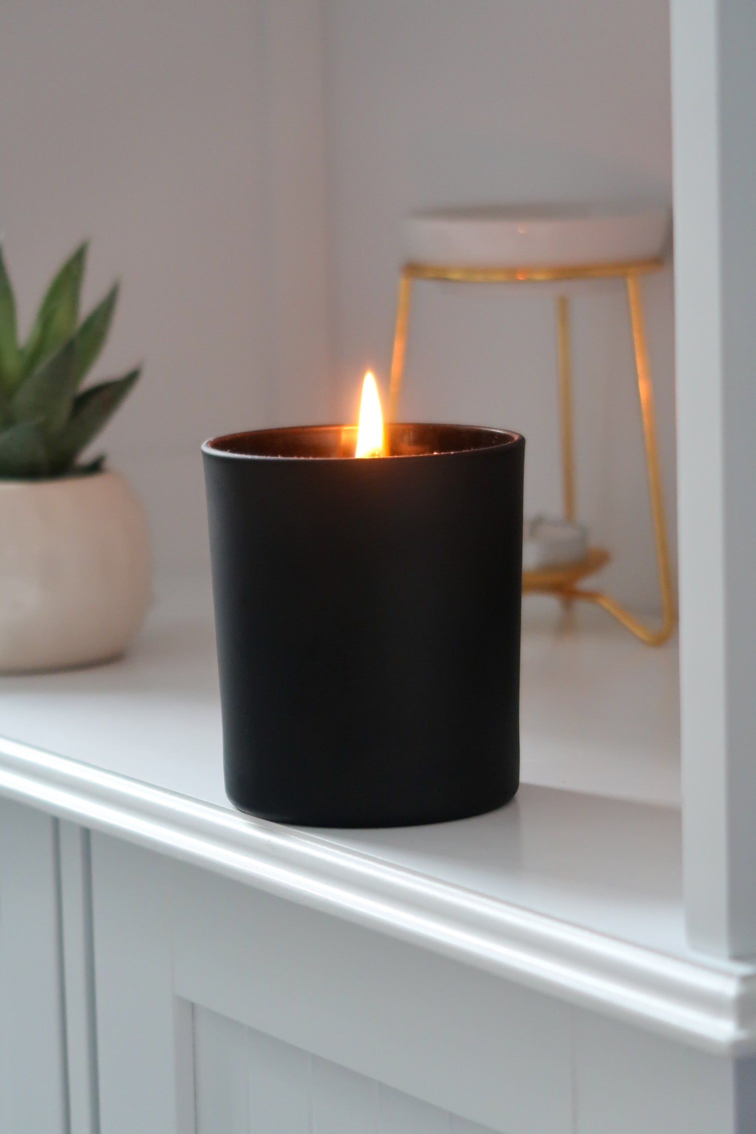 A lit 30cl Black Matte Candle from Timeless Aromas Ltd, showcasing the elegant design of a hand poured candle perfect for home fragrance. This ceramic jar candle adds a touch of style while being part of a pack of 6, making it an ideal gift. Features include a matte finish and blank label for customisation, perfect for wholesale. The white candle inside enhances the overall aesthetic.