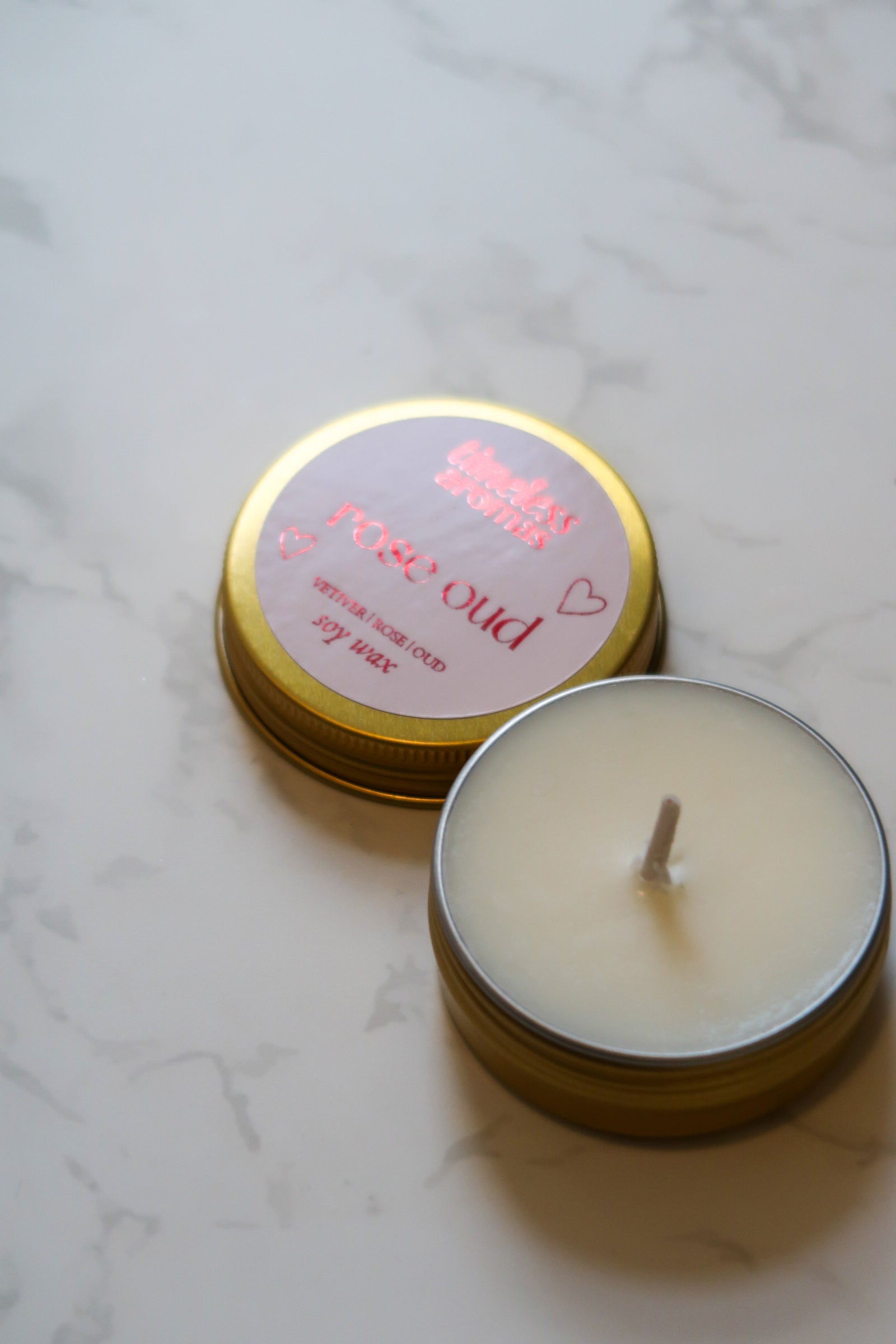 Close-up view of the Timeless Aromas Ltd Rose Oud Mini Gold Tin Candle with a lit wick, ideal for adding a romantic touch during travel or at home.