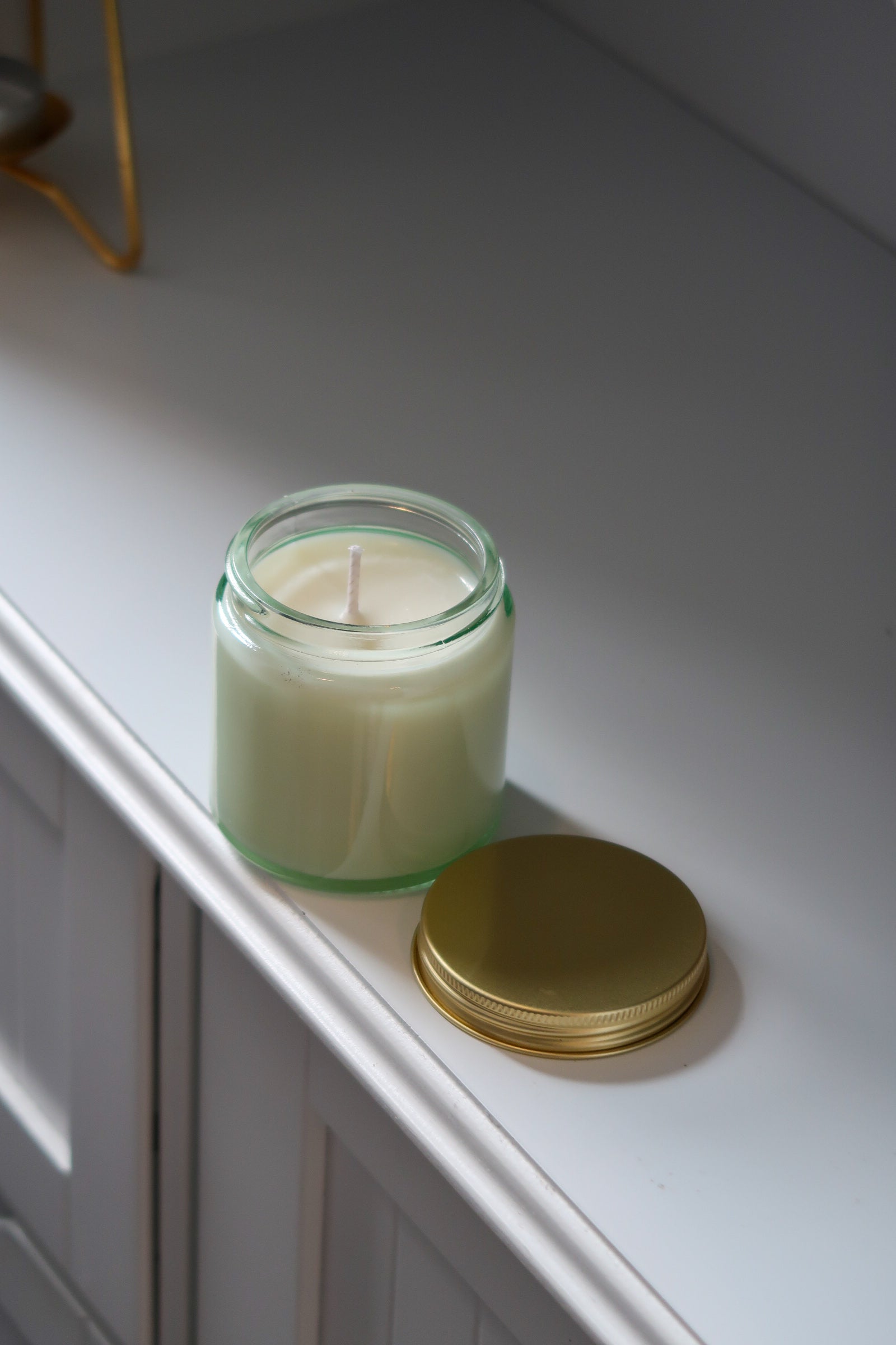 A close-up of a 120g Clear Glass Gold Lid Candle by Timeless Aromas Ltd, highlighting its white candle wax ready to be lit. This hand poured candle is part of a pack of 6, featuring a gold lid and perfect for home fragrance or gifting. Ideal for wholesale, it includes a blank label for personalization.