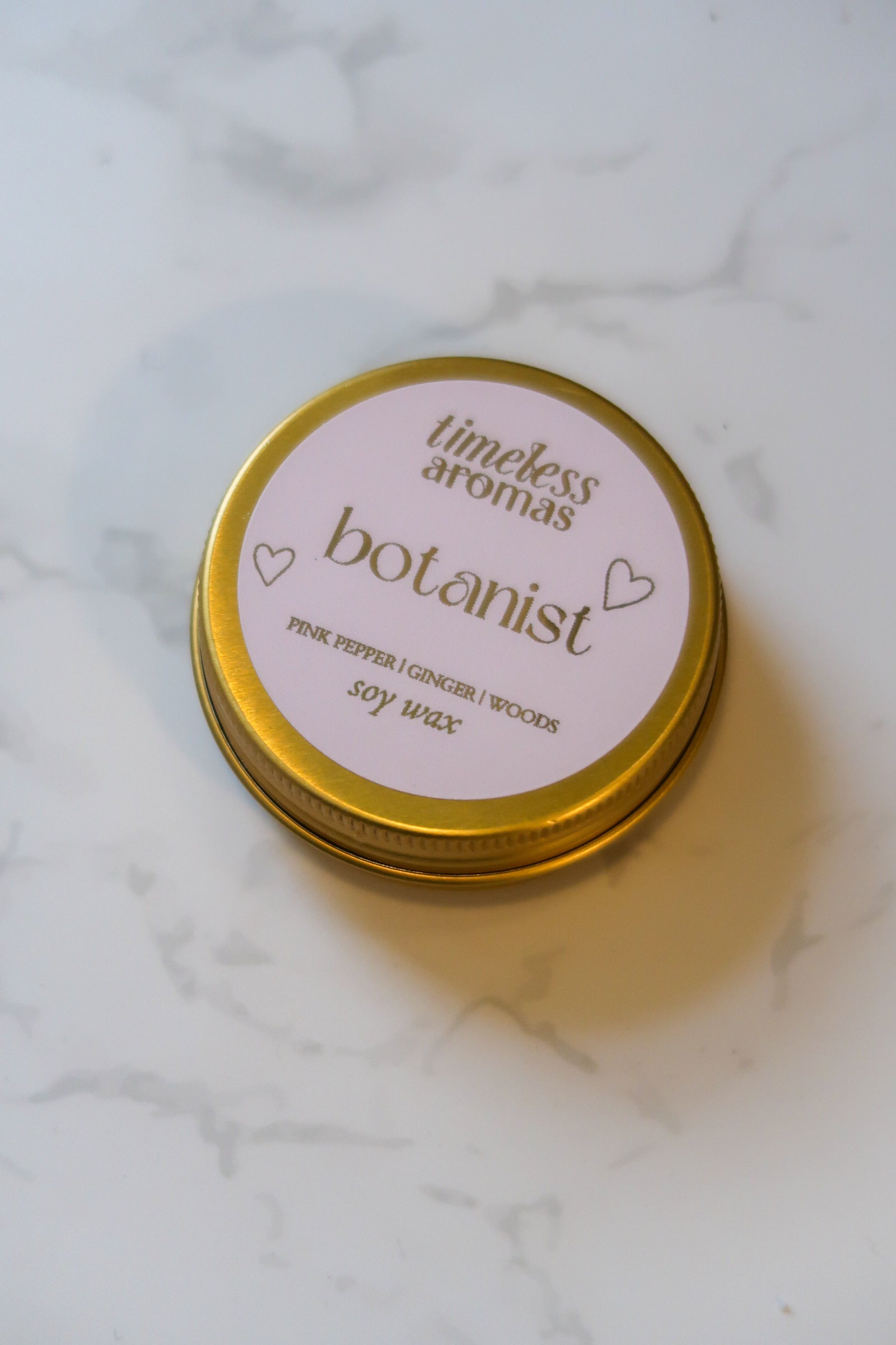 Close-up of the Botanist Mini Gold Tin Candle's label by Timeless Aromas Ltd, featuring the scent profile and a charming design, making it an ideal floral and woody mini gold tin candle.