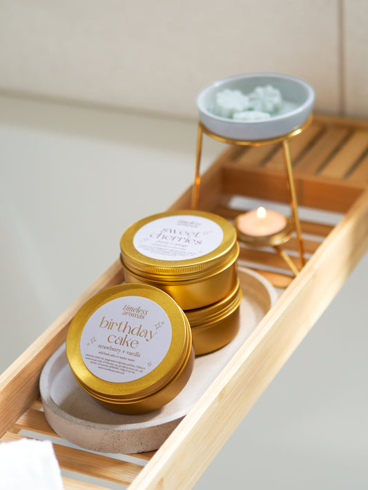 Stylish display of Timeless Aromas Birthday Cake Gold Tin Bath Salts – Strawberry Sweets on a wooden tray, promoting relaxation with bath salts for relaxation.