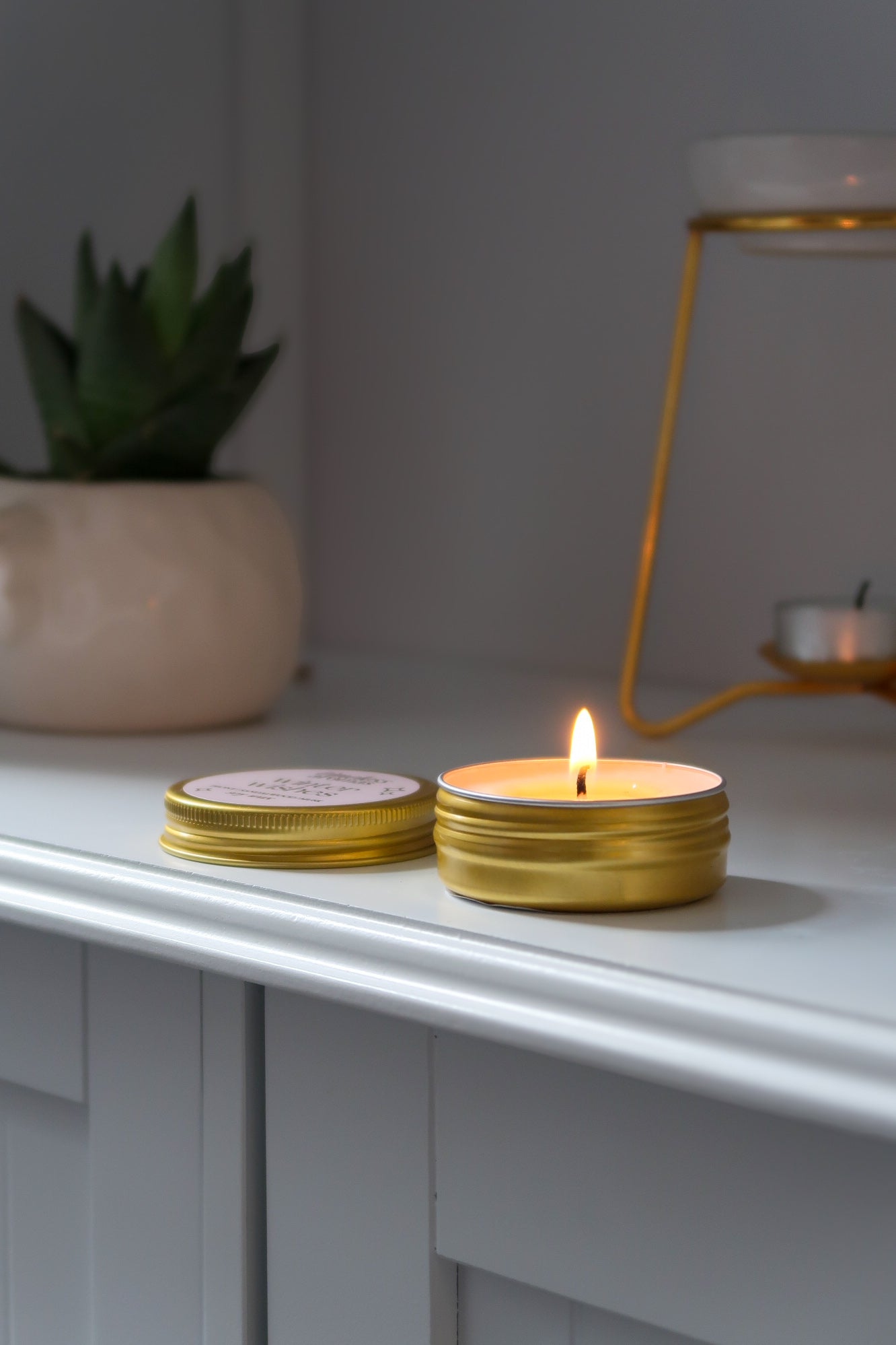 A beautifully lit 30g Gold Tin Candle from Timeless Aromas Ltd, highlighting the warm glow of hand poured candles. This candle is part of a pack of 6, perfect for elevating your home fragrance. The elegant gold lid adds a touch of luxury, making it a great gift option. Ideal for those looking for a ceramic feel in their decor, this candle features a blank label, offering versatility. Perfect for wholesale, these jar candles make any space inviting with delightful scents.