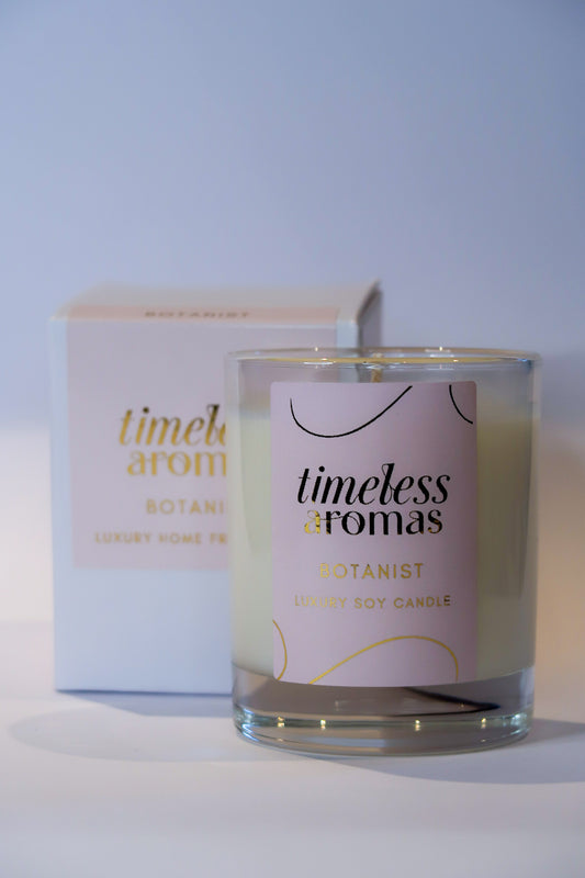 Timeless Aromas Botanist Handcrafted Luxury Candle in a clear glass jar, showcasing its elegant label and fresh scent, perfect for brightening up any space.