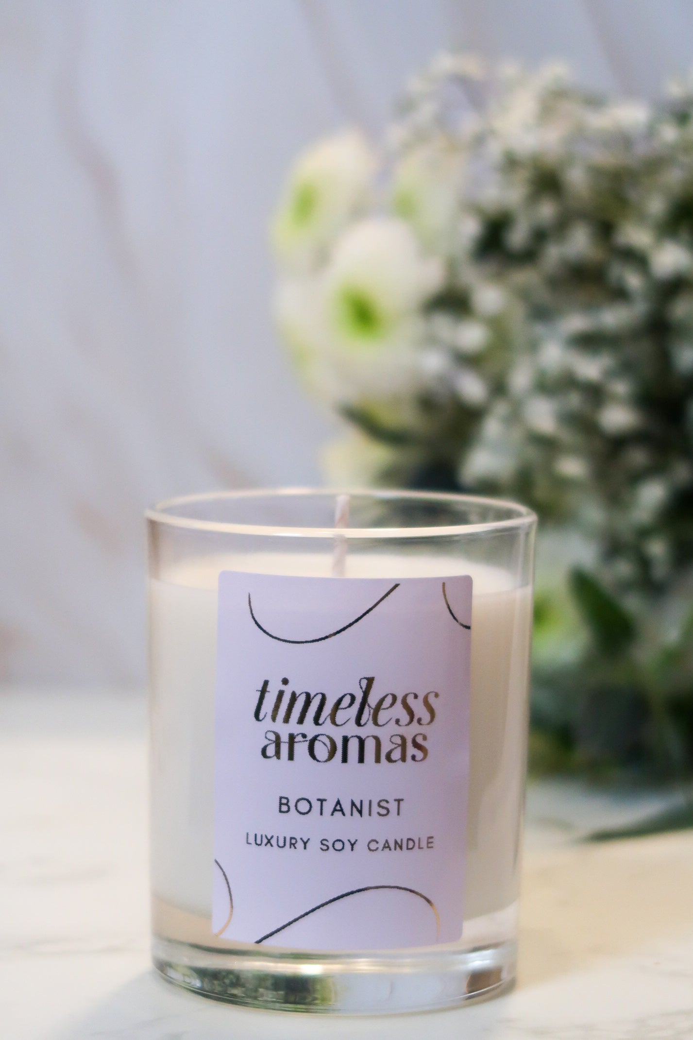 Timeless Aromas Botanist Handcrafted Luxury Candle with a stylish design, set against delicate floral decor, perfect for home ambiance.