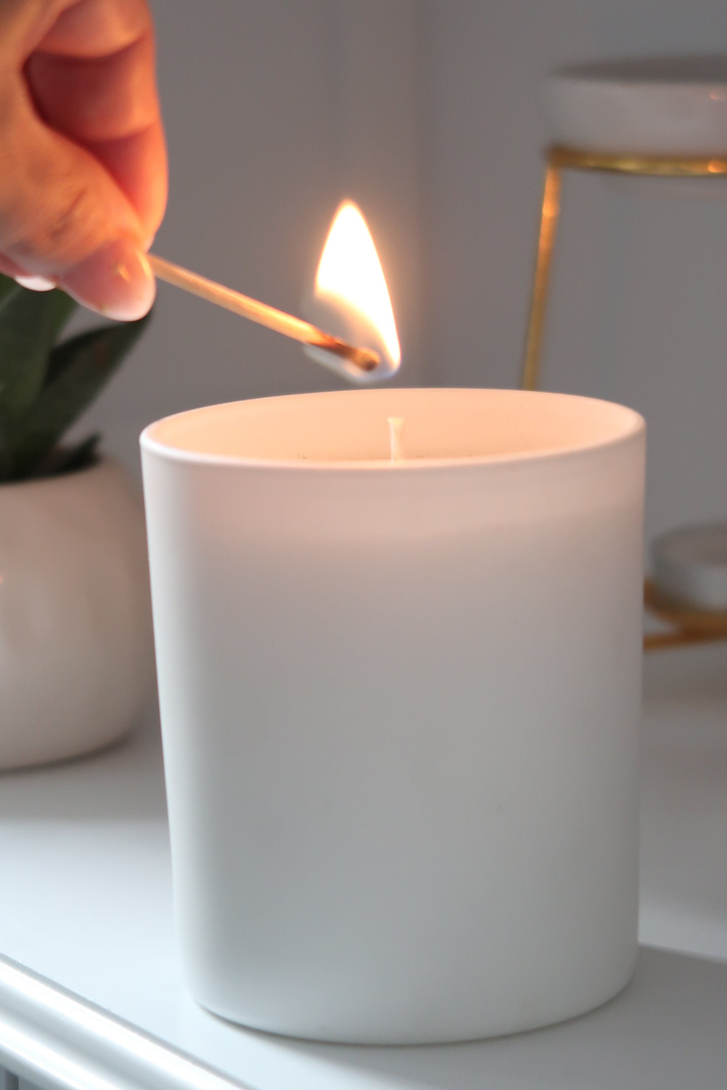 A hand reaching to light a 30cl White Matte Candle from Timeless Aromas Ltd. This hand poured candle offers a soothing home fragrance in a matte ceramic jar, making it a great gift option within a pack of 6. Blank label candles for businesses 