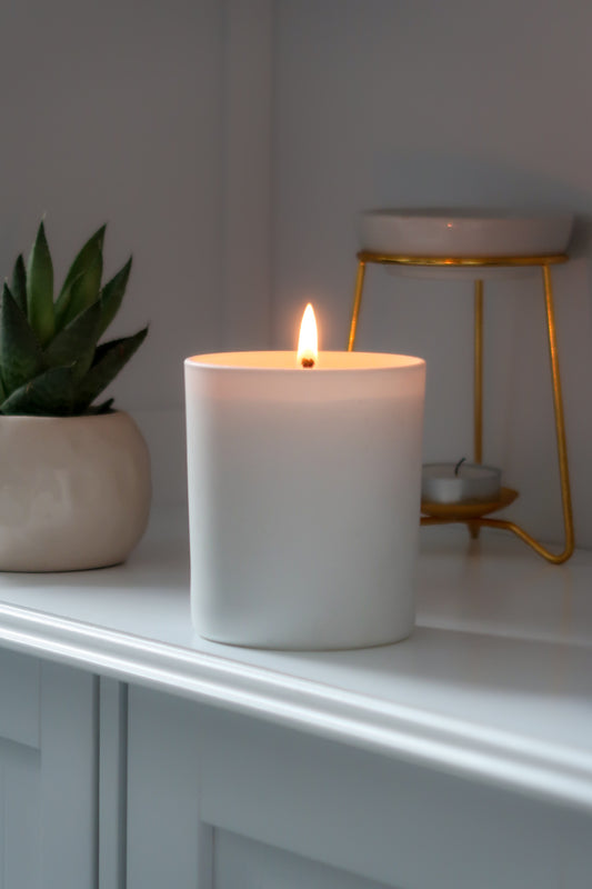 A lit 30cl White Matte Candle from Timeless Aromas Ltd, showcasing hand poured candles perfect for home fragrance. Ideal as a gift, this ceramic jar candle is part of a pack of 6, featuring a blank label design that complements any decor. Blank label candles for businesses 