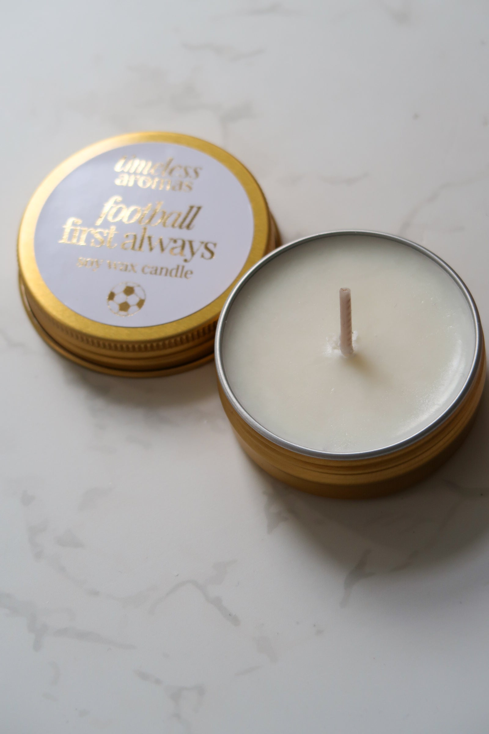 Close-up of the Timeless Aromas Ltd Football First Always Mini Gold Tin Candle showcasing its clean white wax and sophisticated design, an ideal present for passionate football fans. A perfect addition to special celebrations like the World Cup or Father's Day, suitable for Arsenal and Chelsea enthusiasts.