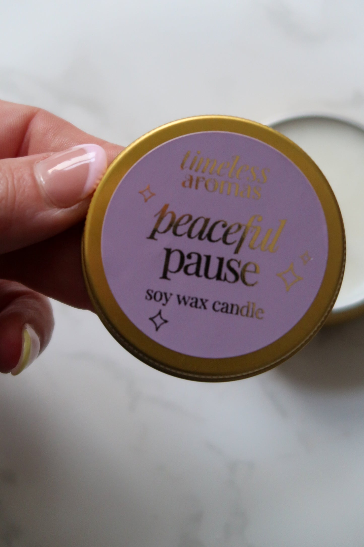 A hand holding Timeless Aromas Ltd Peaceful Pause Mini Gold Tin Candle, highlighting its calming scent and elegant packaging.
