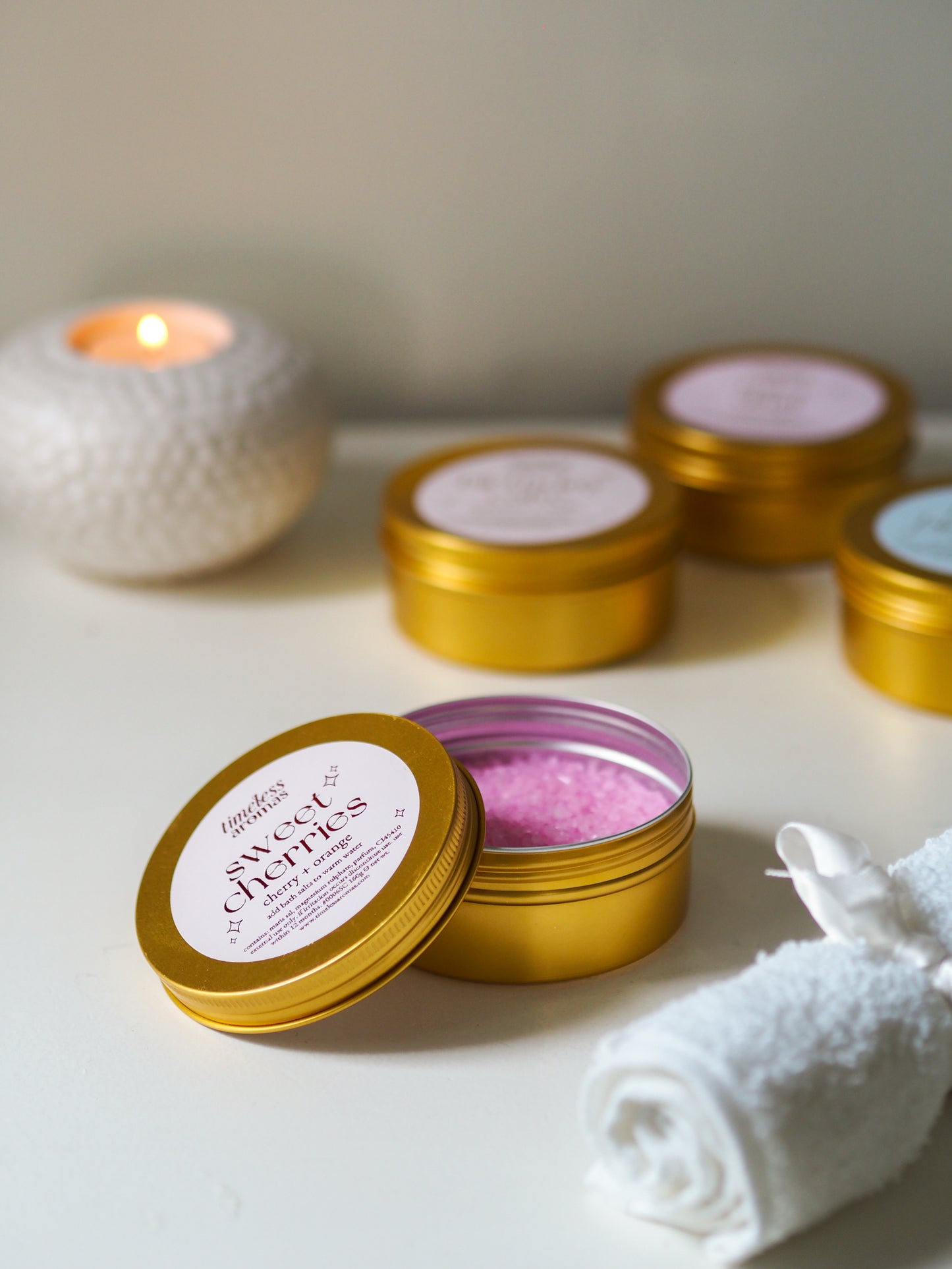 Open tin of Sweet Cherries Gold Tin Bath Salts by Timeless Aromas, revealing the pink salts inside, an essential for creating a soothing bath environment. The perfect choice of bath salts for relaxation.