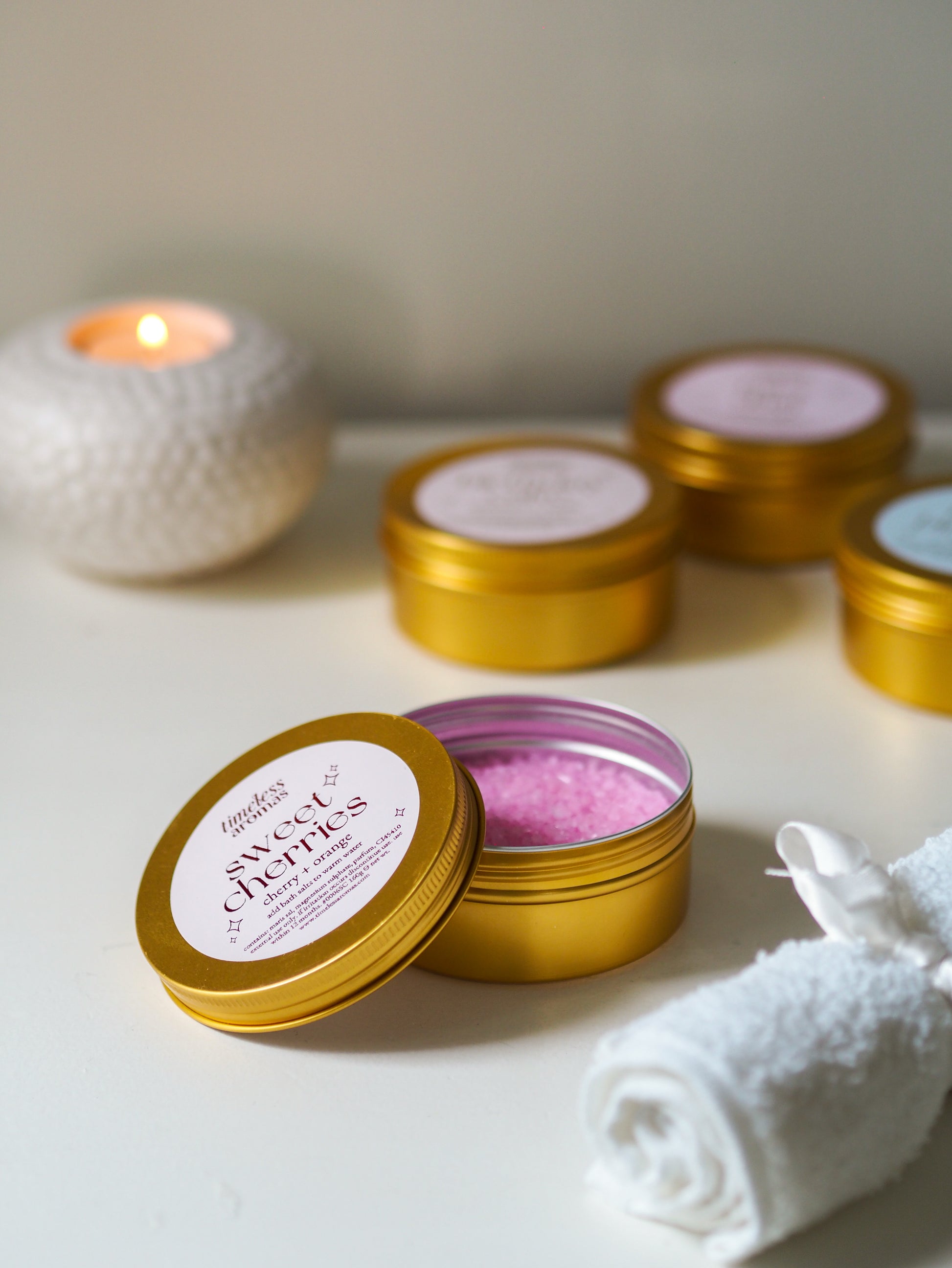 Open tin of Sweet Cherries Gold Tin Bath Salts by Timeless Aromas, revealing the pink salts inside, an essential for creating a soothing bath environment. The perfect choice of bath salts for relaxation.
