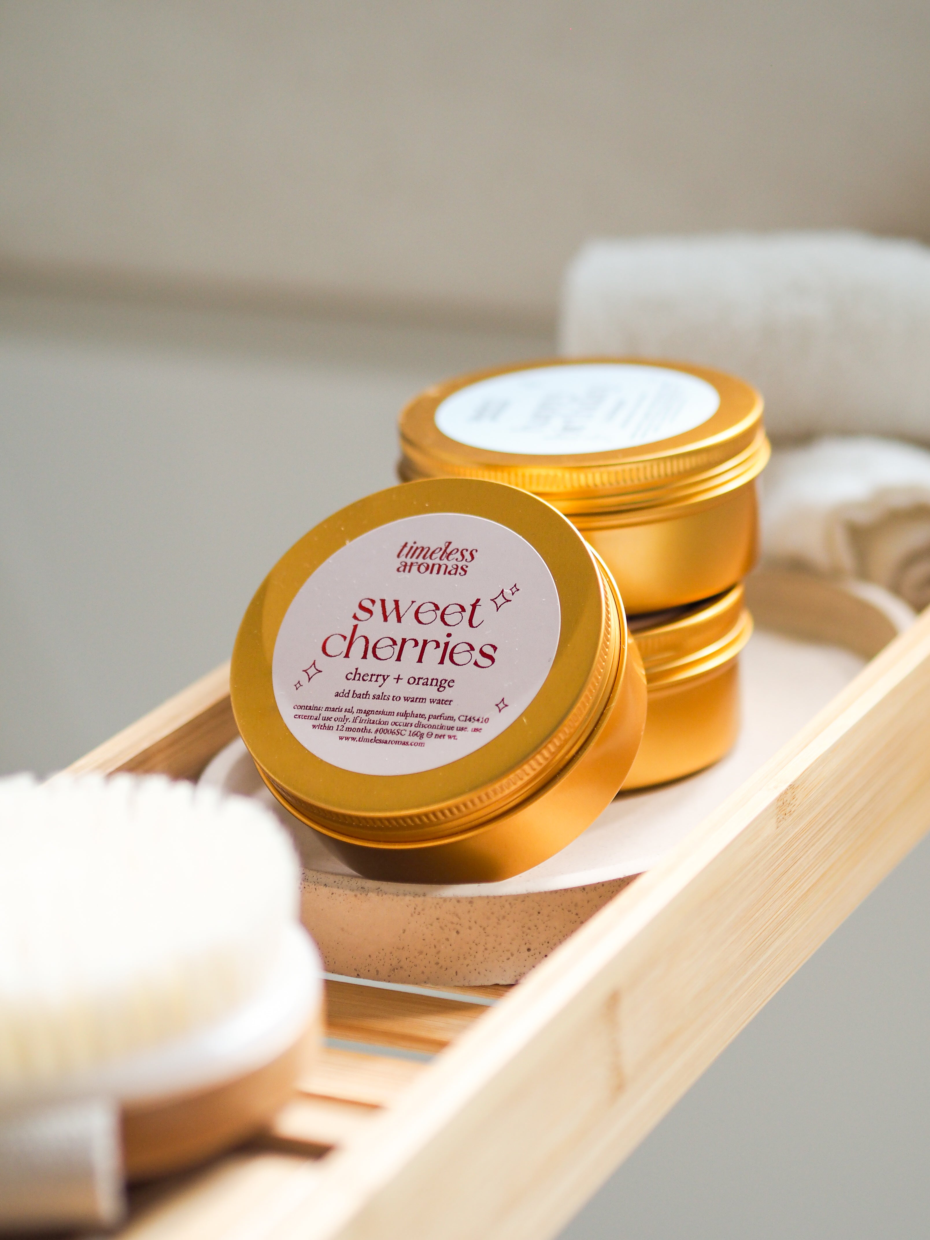Beautifully arranged Sweet Cherries Gold Tin Bath Salts by Timeless Aromas, showcasing the vibrant tins perfect for a relaxing bath experience. Ideal bath salts for relaxation.
