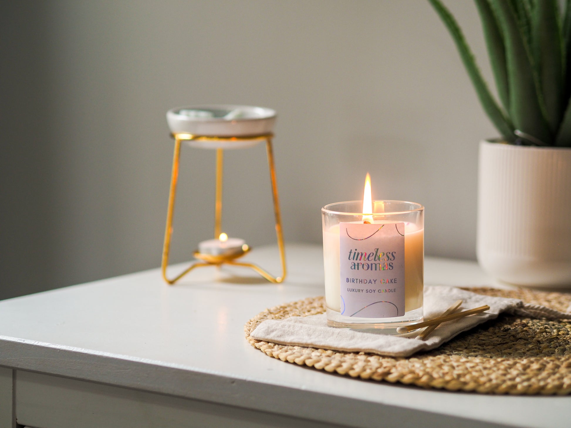 Timeless Aromas Birthday Cake Scented Candle glowing brightly on a table beside a golden tea light holder, adding a festive touch to home decor.