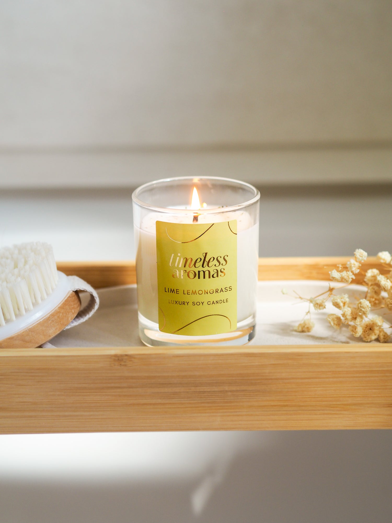 A lit Lime Lemongrass Luxury Candle by Timeless Aromas on a bamboo tray, surrounded by a natural brush and dried flowers, enhancing the refreshing ambiance.