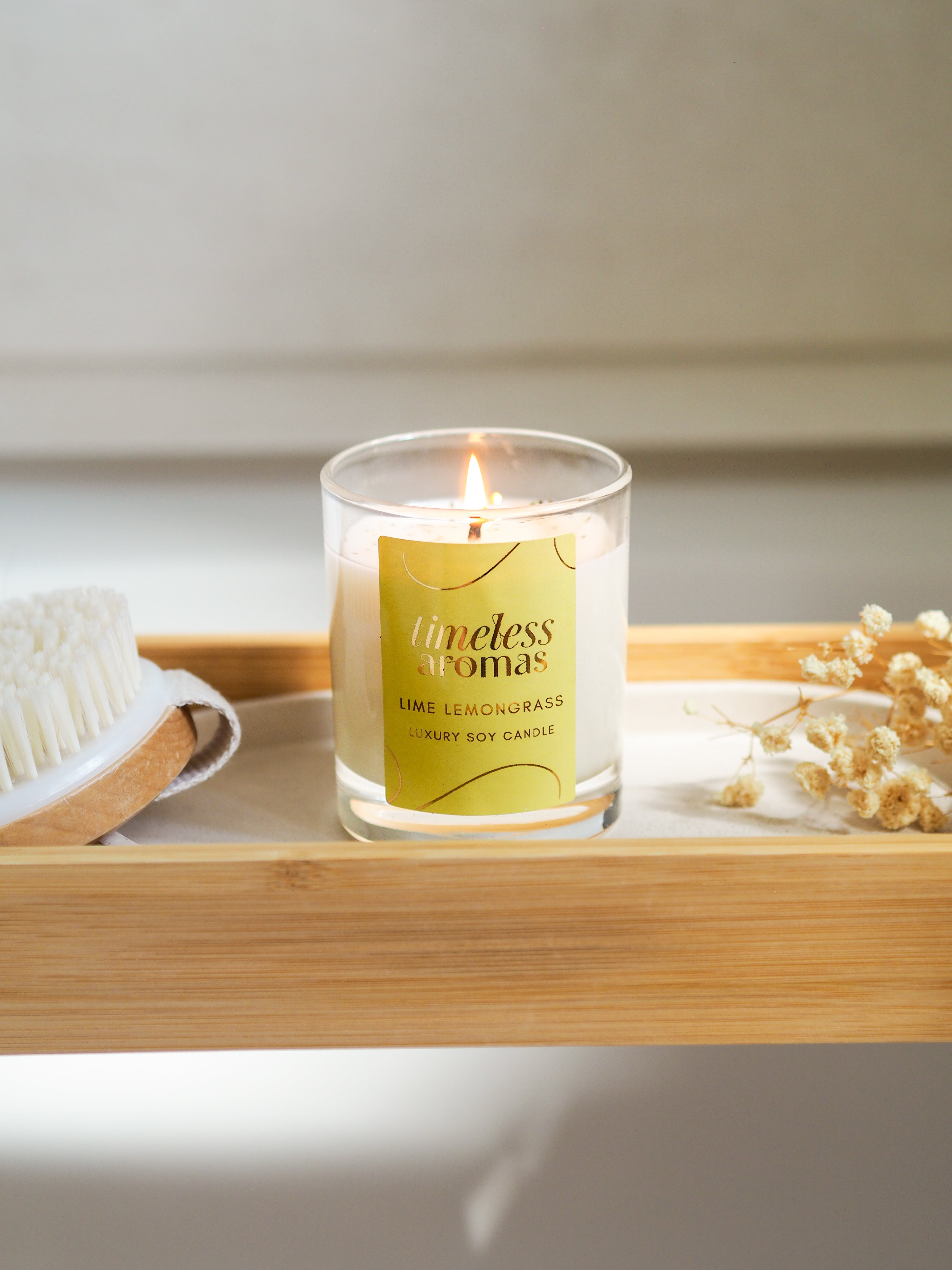 A lit Lime Lemongrass Luxury Candle by Timeless Aromas on a bamboo tray, surrounded by a natural brush and dried flowers, enhancing the refreshing ambiance.