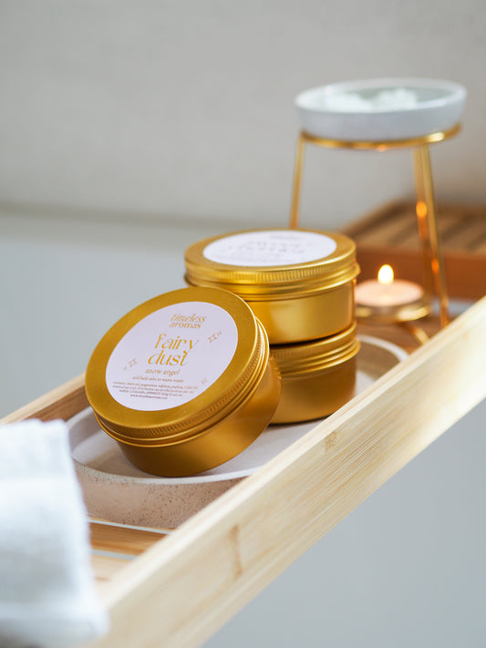 Fairy Dust Gold Tin Bath Salts by Timeless Aromas, beautifully displayed on a wooden bath tray, perfect for your self-care routine. These luxurious bath salts for relaxation, infused with the enchanting Snow Angel fragrance, offer a soothing experience for the mind and body.