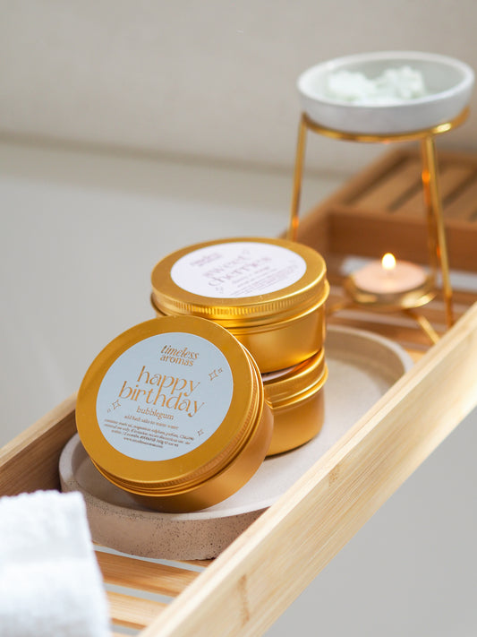 Happy Birthday Gold Tin Bath Salts by Timeless Aromas, featuring vibrant golden tins on a bamboo tray, perfect bath salts for relaxation with a bubblegum fragrance.