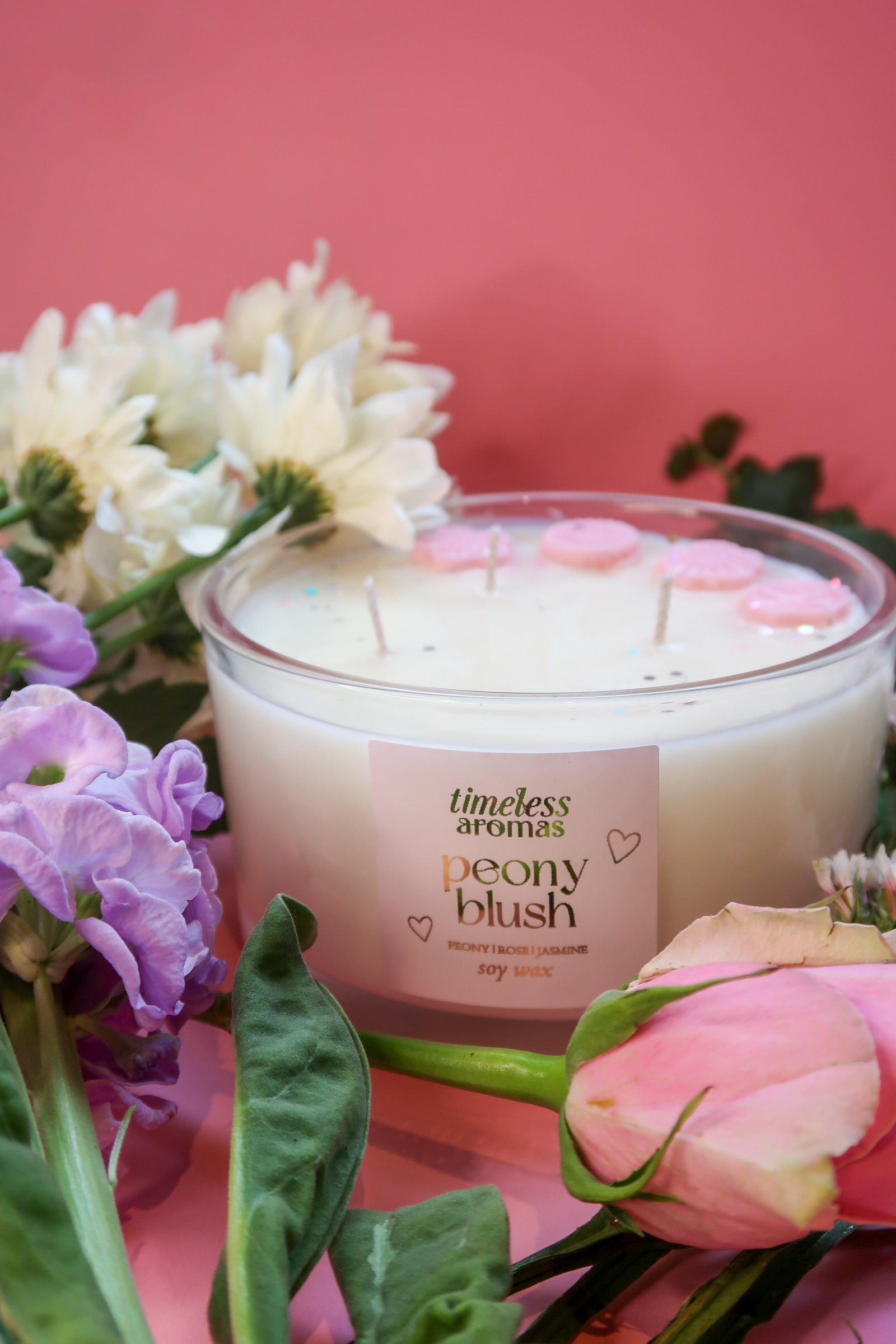 Timeless Aromas Peony Blush Large Candle featuring three wicks, surrounded by colorful flowers. Perfect luxury decor piece with a delightful scent of peonies, apple, and jasmine.